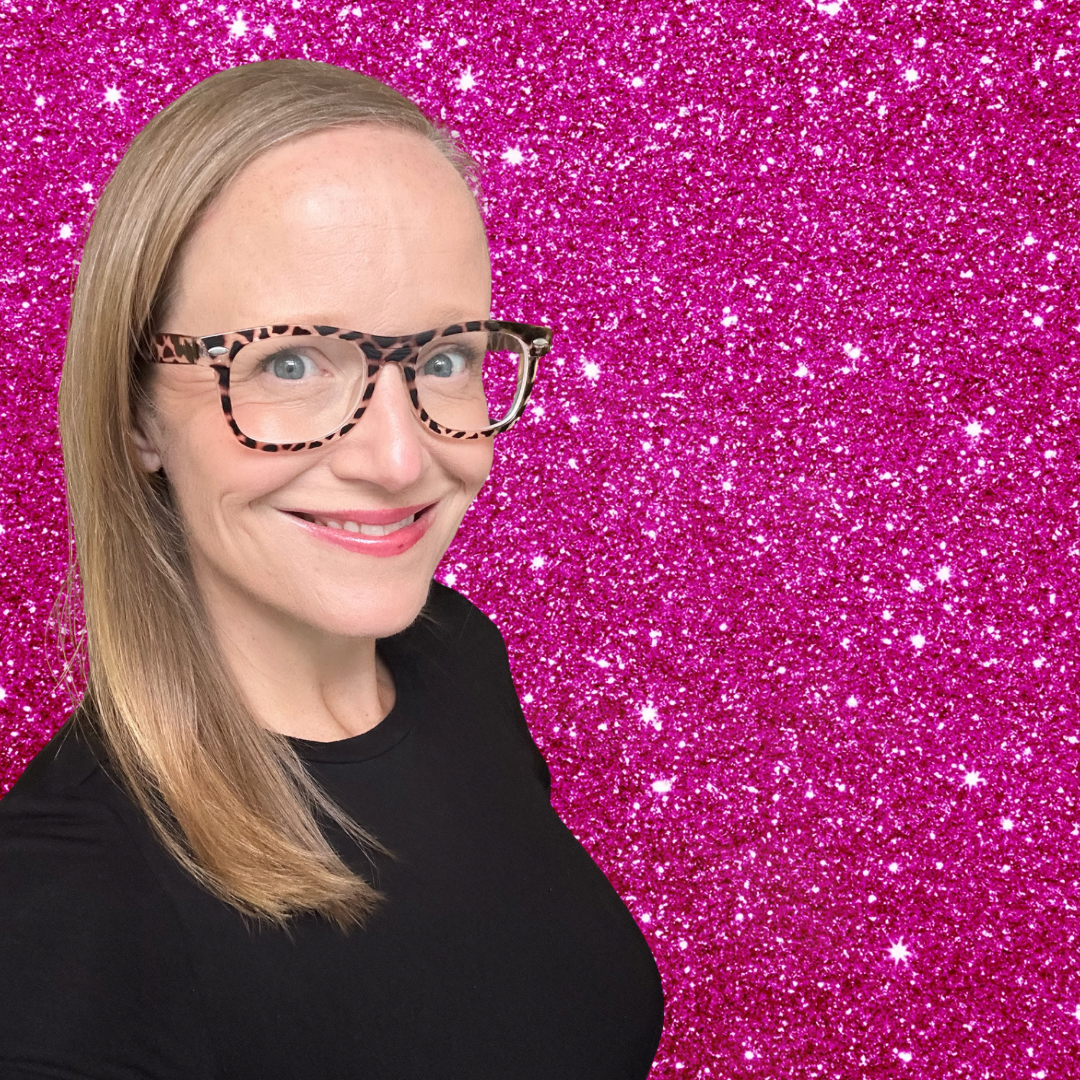 Erin Riska is smiling against a pink glitter background, wearing glasses and a black shirt.