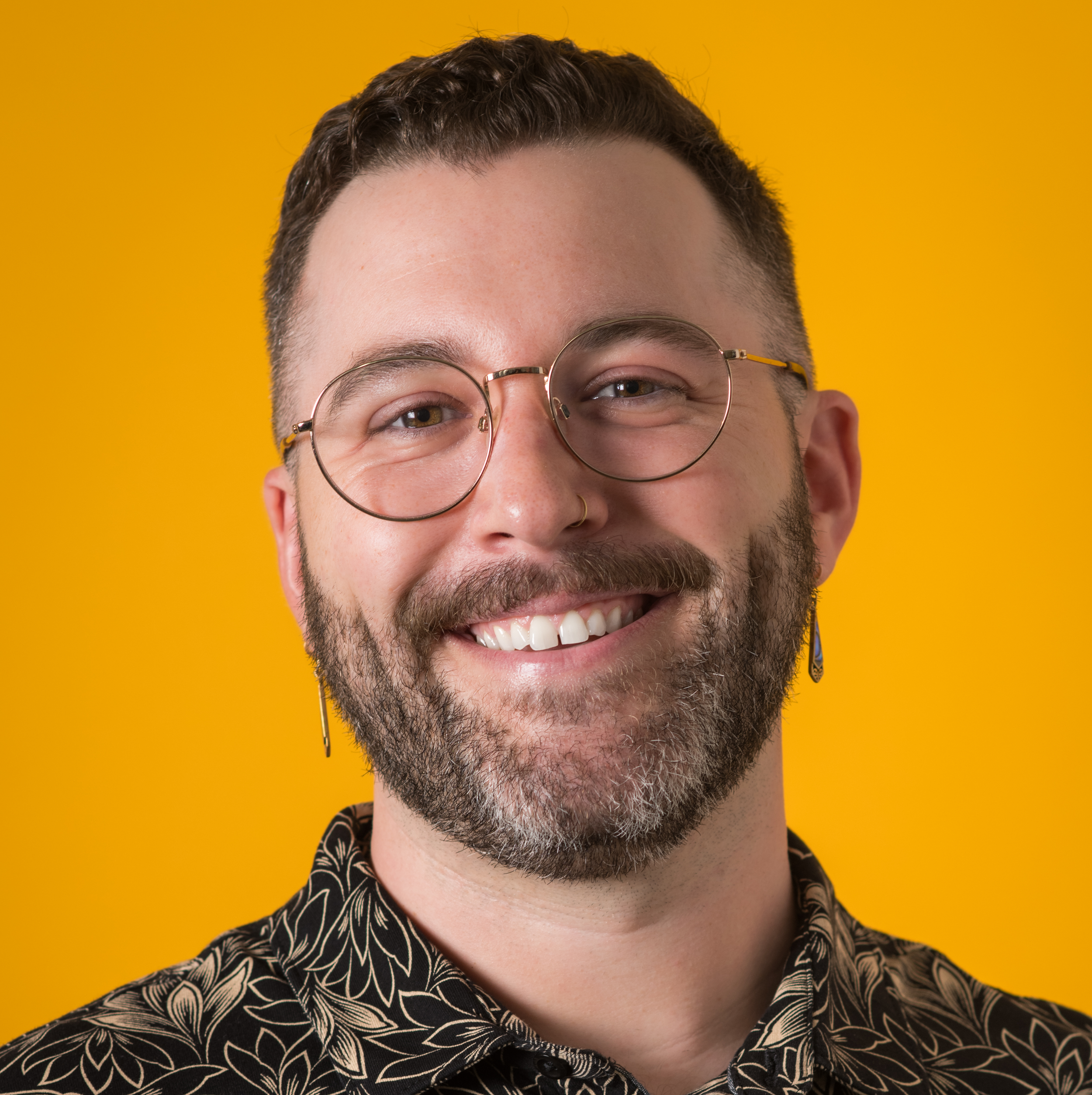 Alex Lahmeye is smiling in glasses against a pure yellow background.