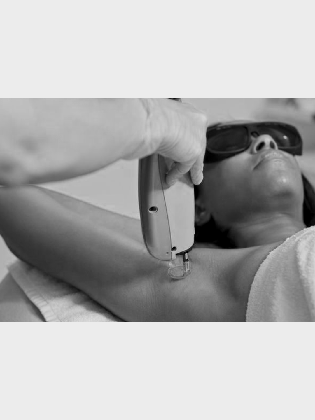 A person lying on a hospital bed, with a towel covering their lower body, is receiving a medical procedure on their leg from a healthcare worker holding a device.