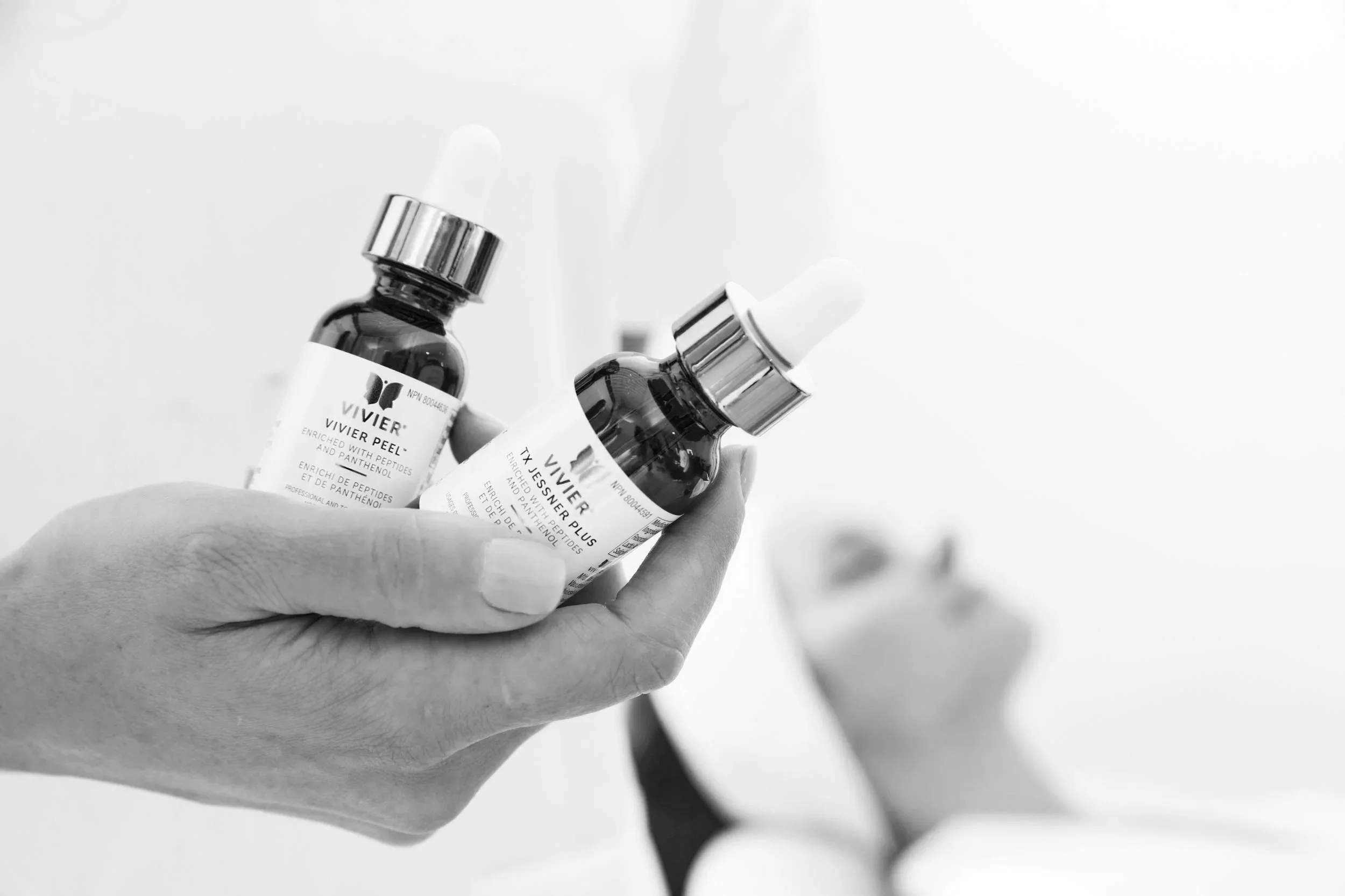A hand holding two small glass bottles with dropper caps, labeled as skincare or cosmetic products.