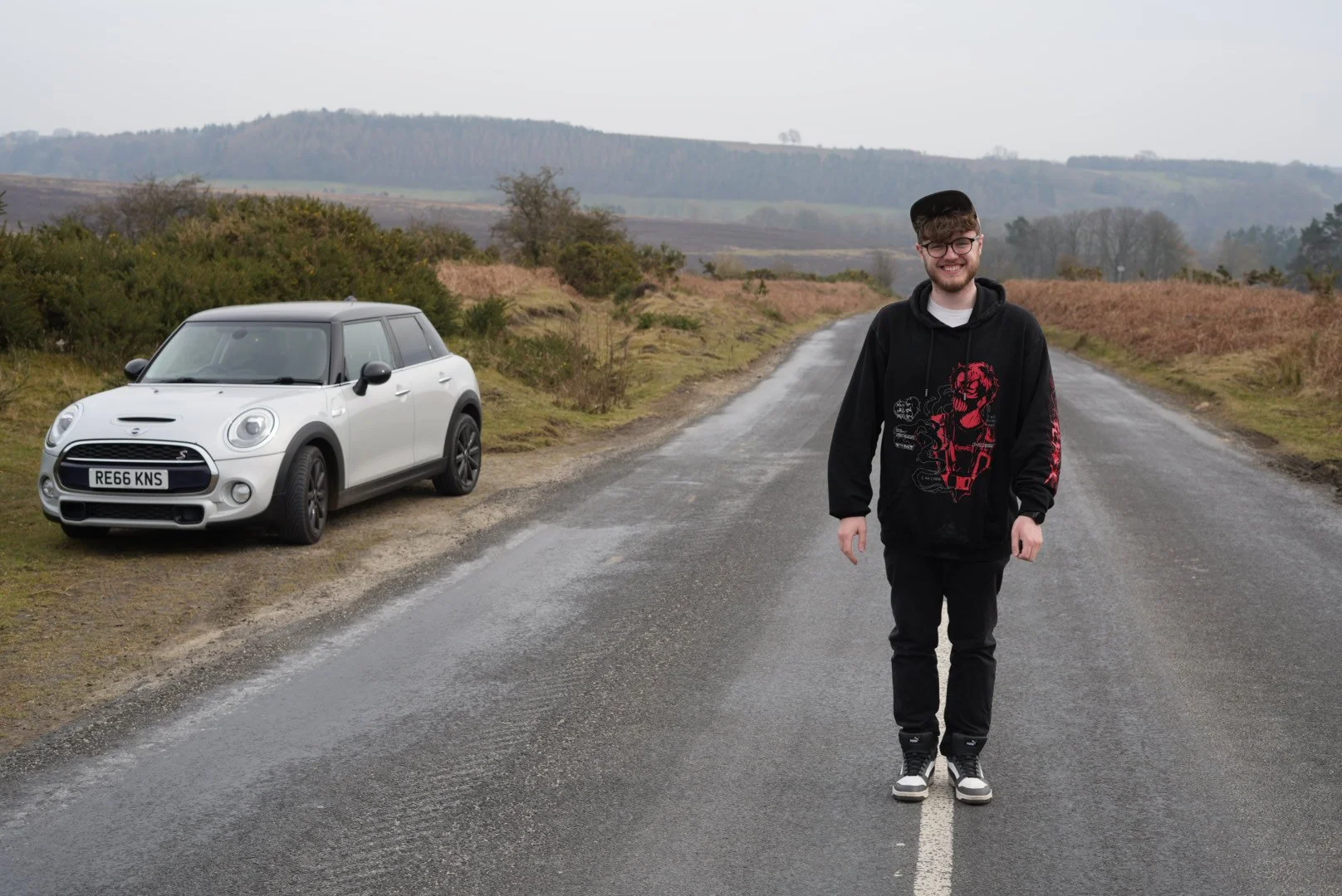 SLT on an open road with a white Mini Cooper parked on the side, set against a rural landscape with hills and bushes.
