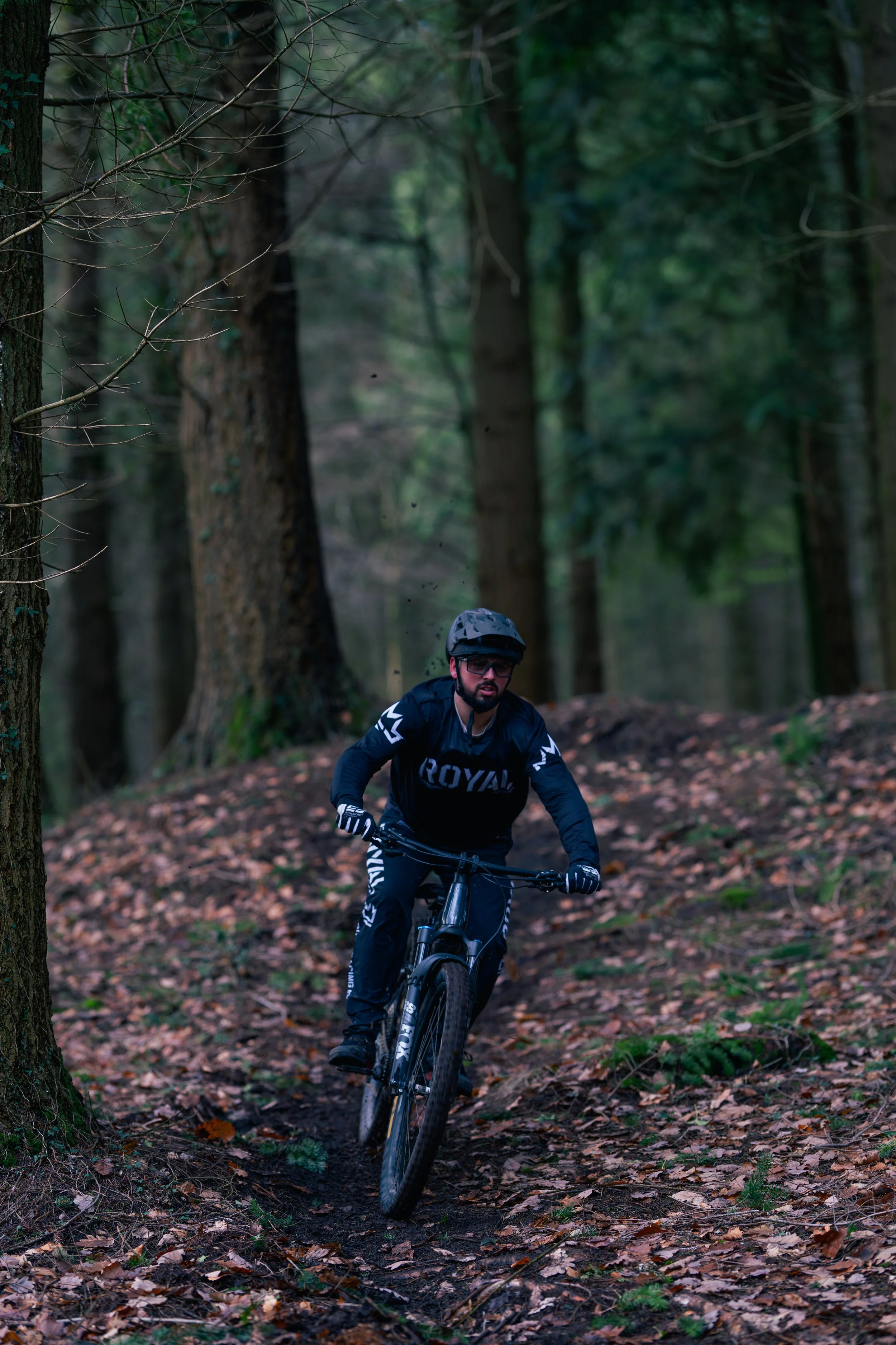 A man mountain biking on a trail through a forest with fallen leaves.