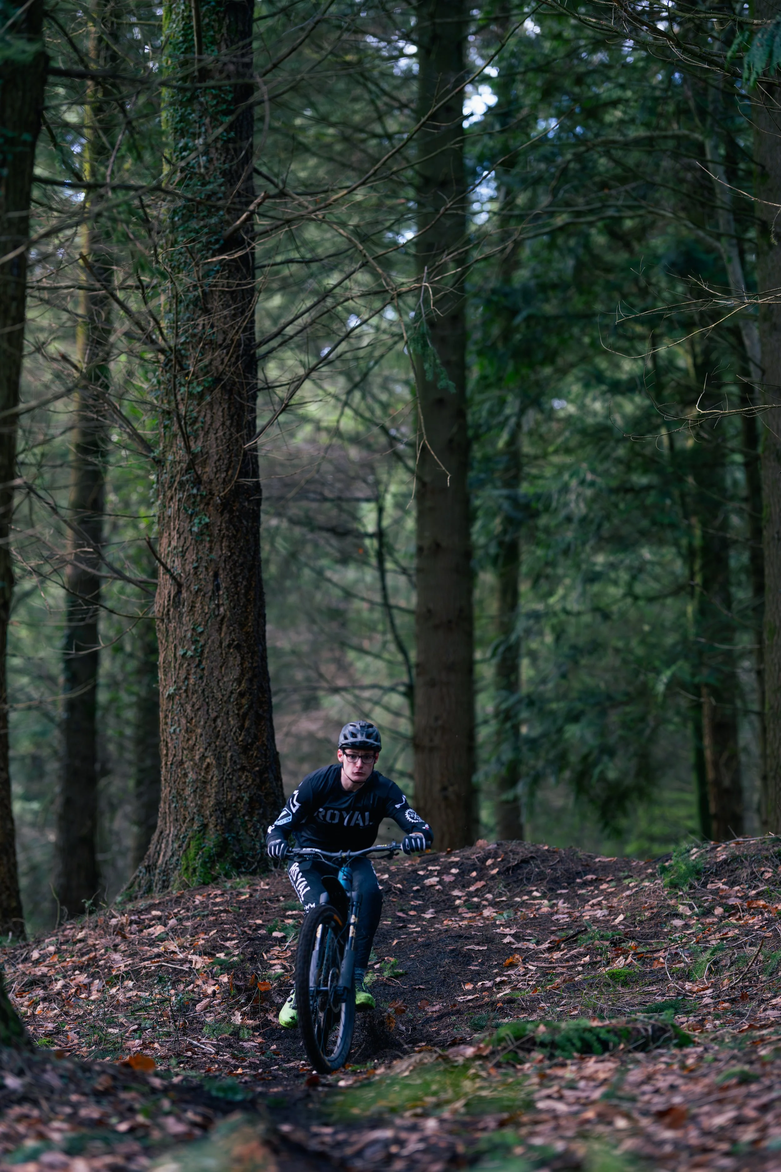A person riding a mountain bike through a forest trail surrounded by tall trees and green foliage.