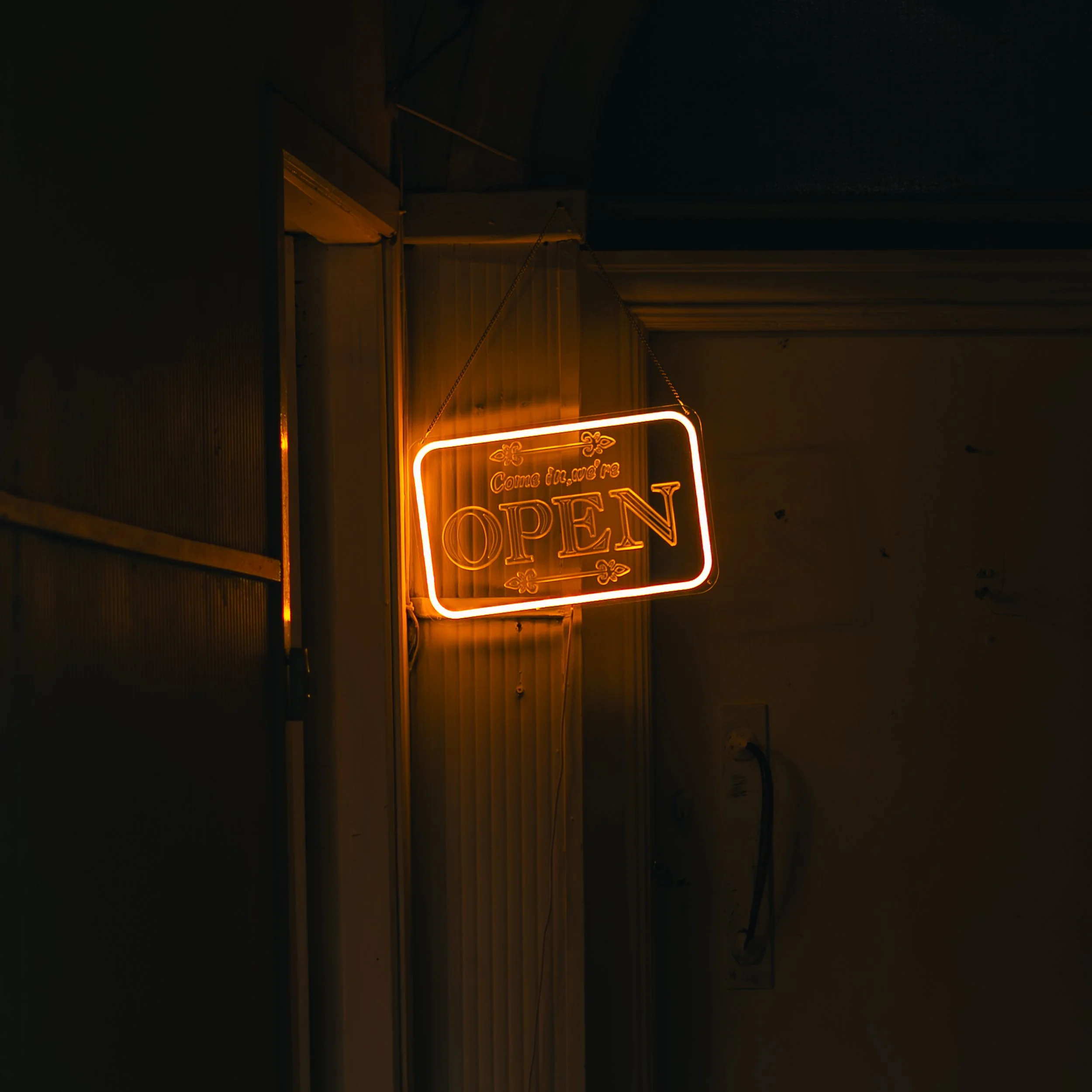 Neon sign reading 'Come in and we're OPEN' hanging on a wall in a dimly lit room.