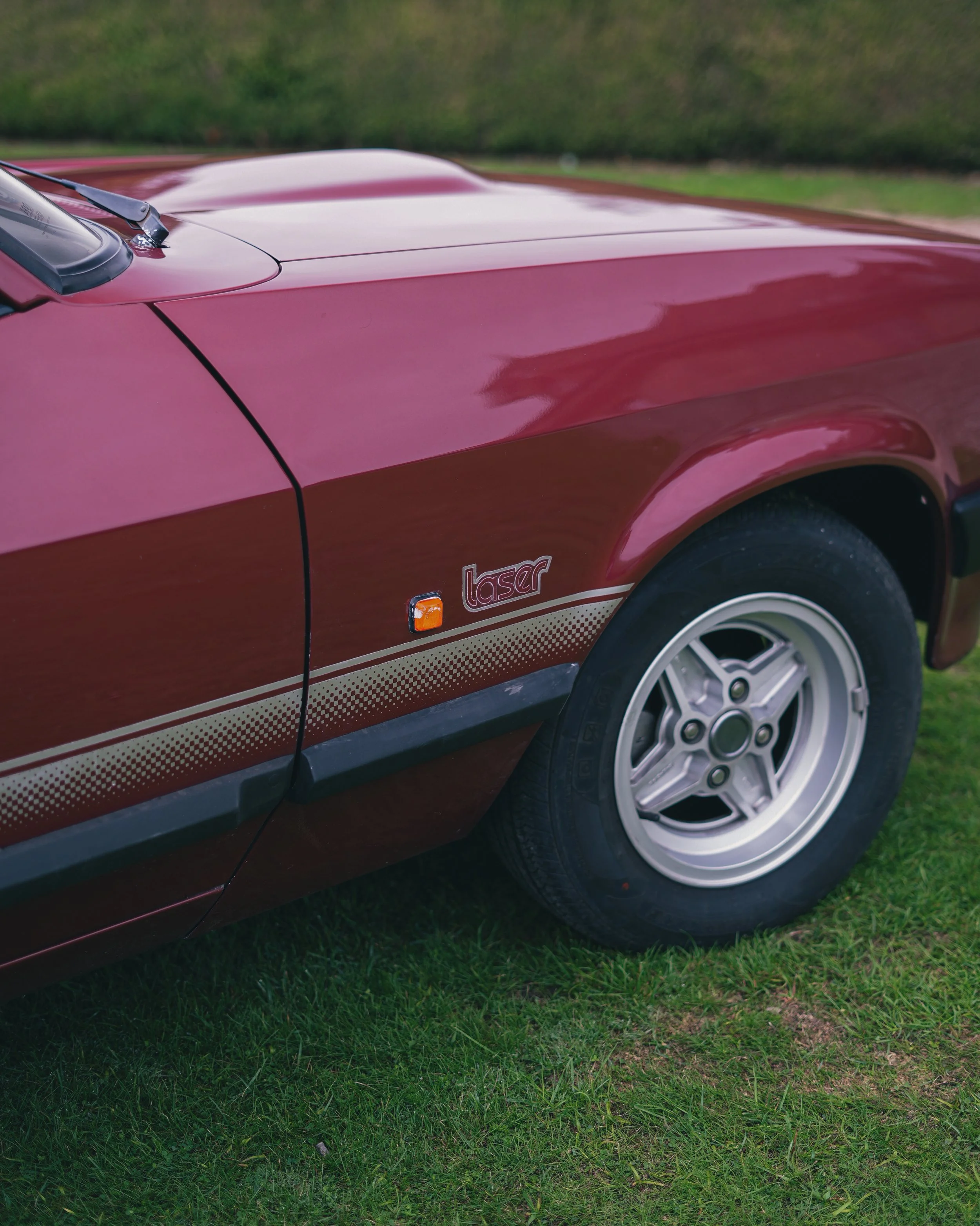 Close-up of a vintage red Ford Capri car with a 'lasar' emblem, parked on grass.