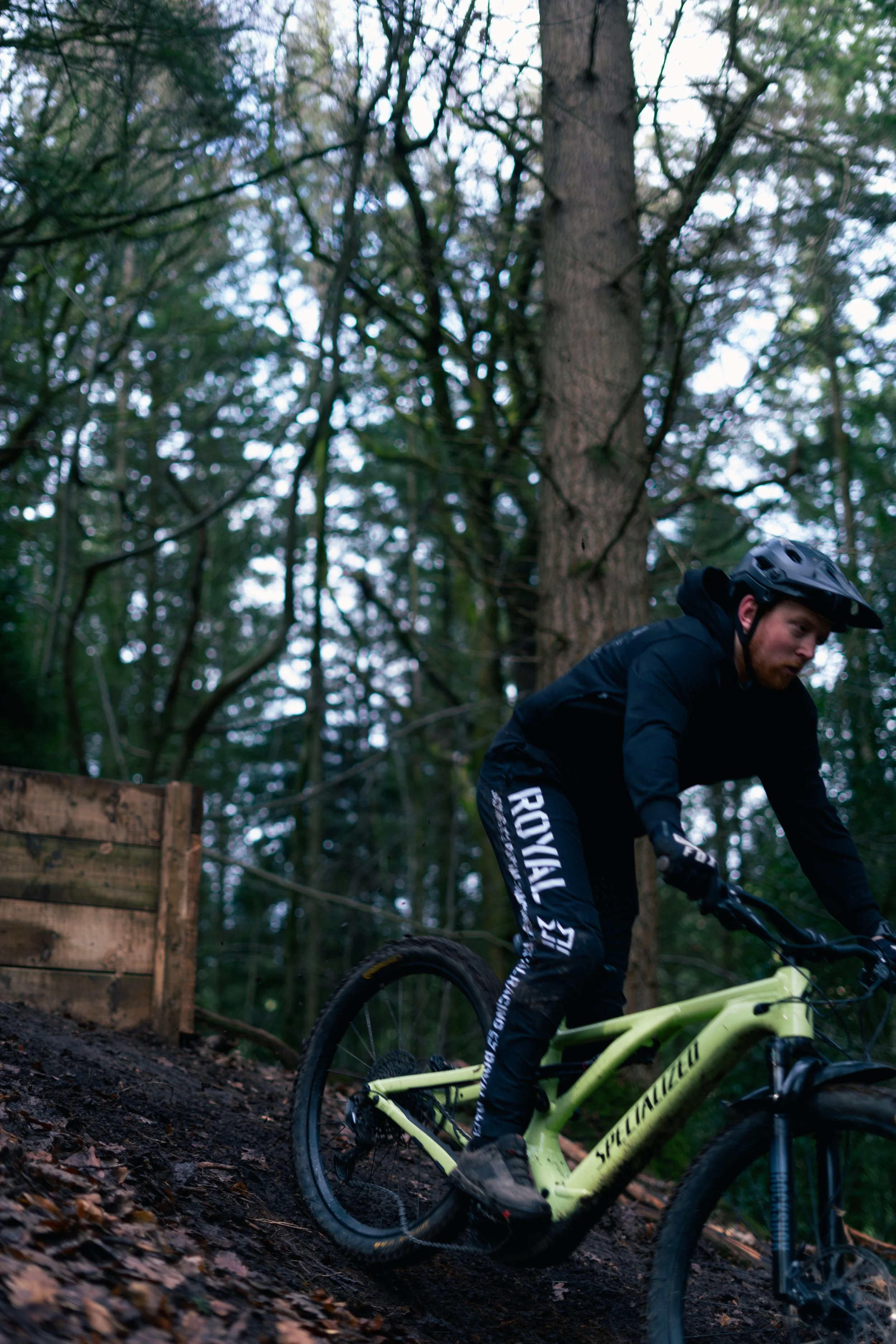 A person mountain biking downhill on a forest trail, wearing a helmet and protective gear.