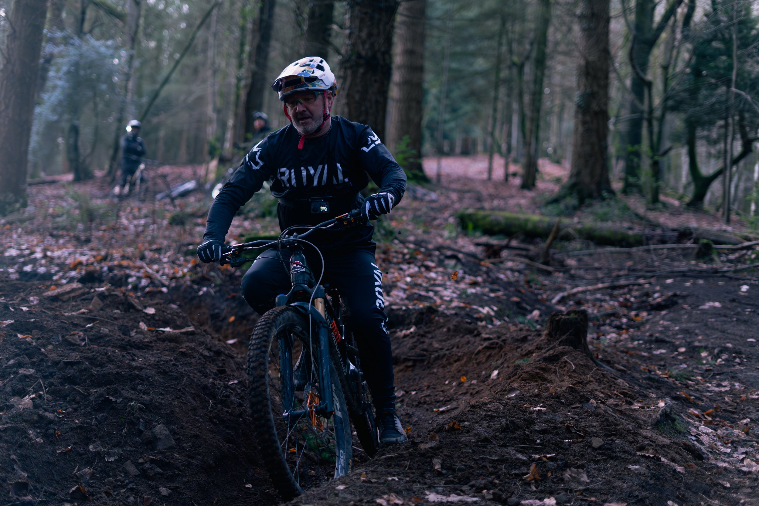 A man riding a mountain bike on a dirt trail through a forest, wearing a helmet and sports gear.