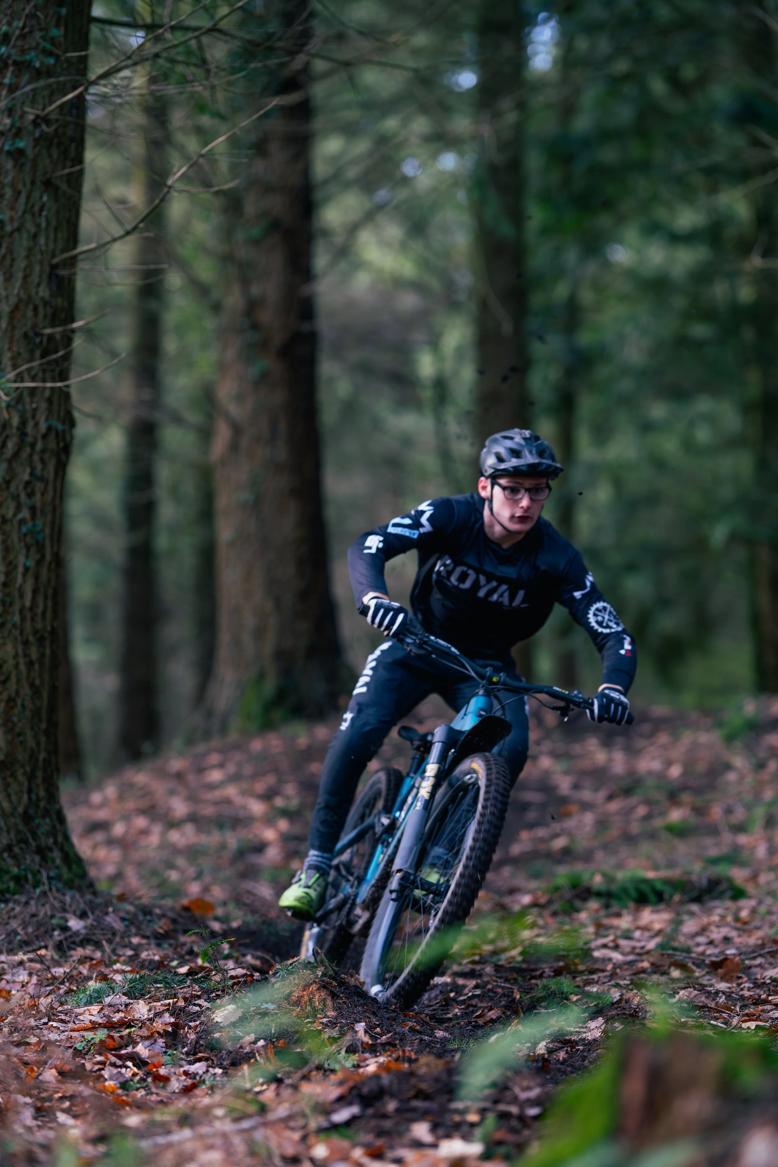 A person mountain biking through a forest trail, wearing a helmet and black cycling gear.