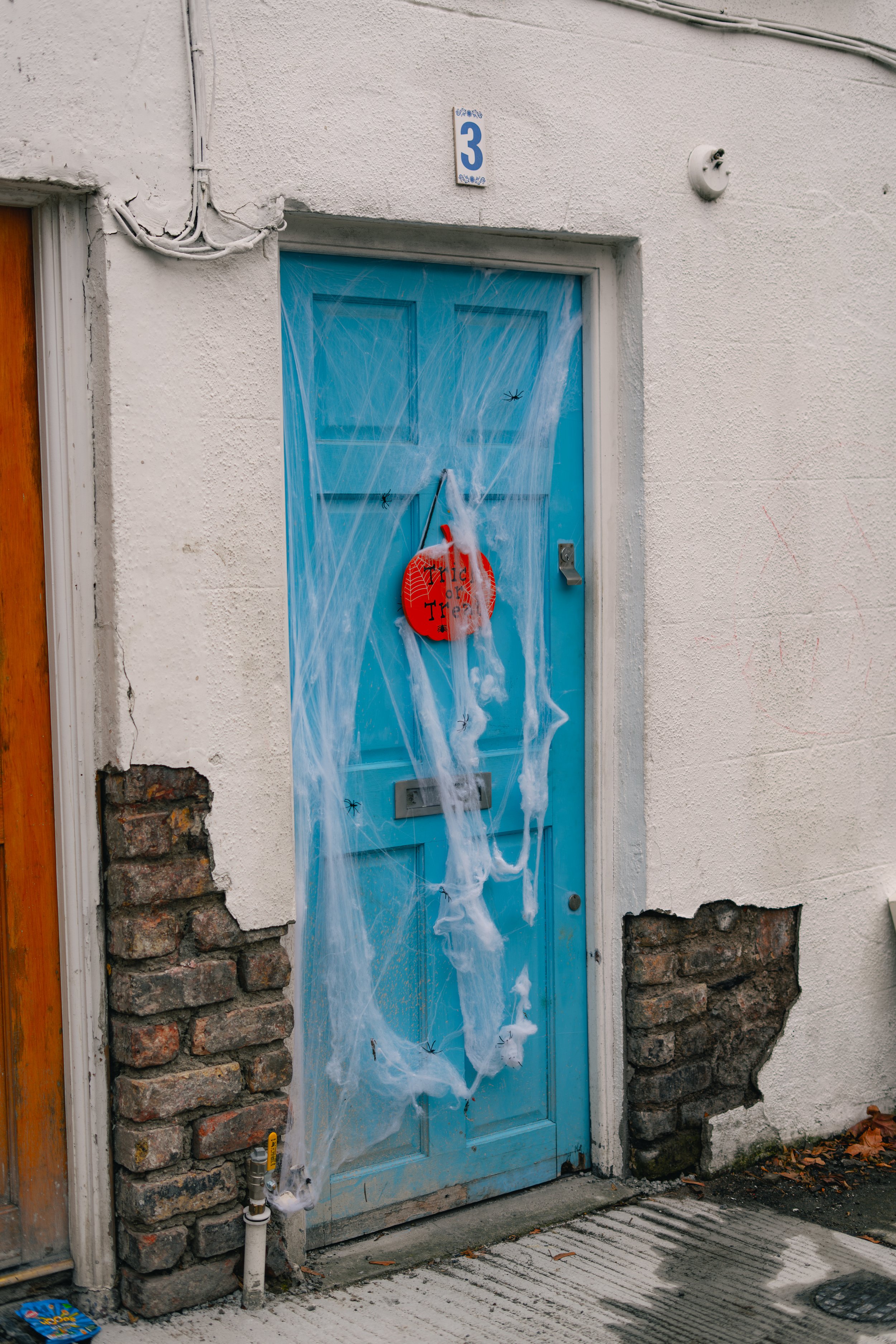 Blue door decorated for Halloween with fake spider webs, plastic spiders, and a red Halloween decoration hanging on the door.