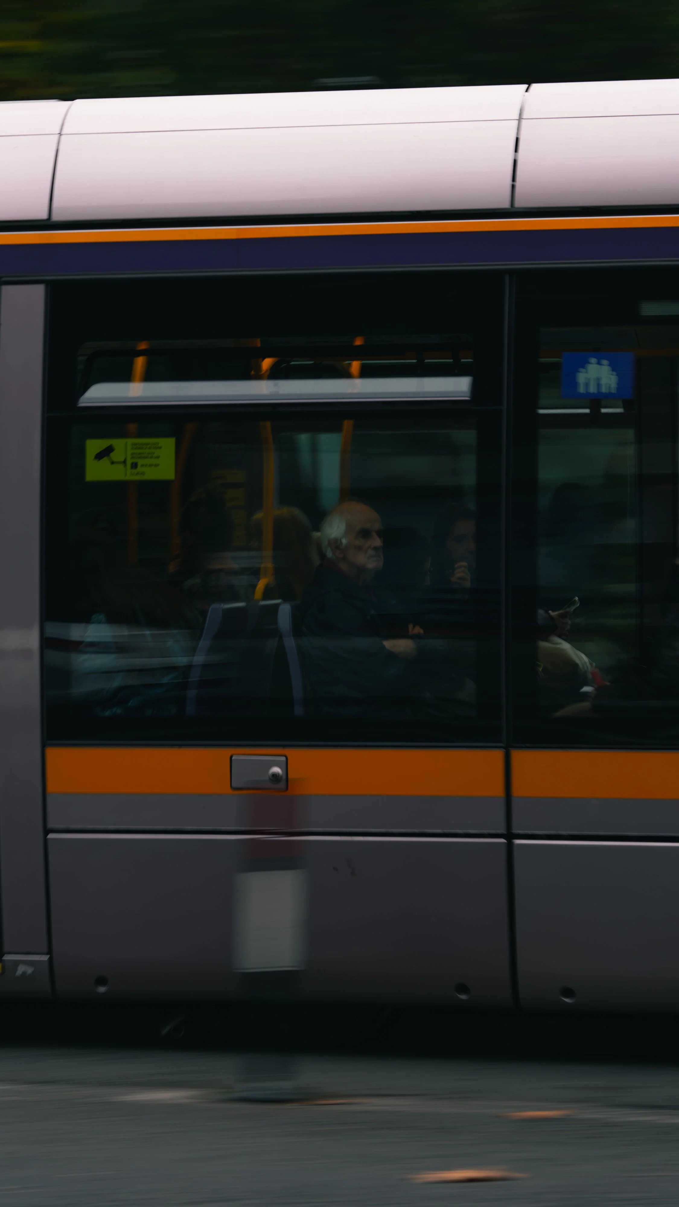 People sitting inside a bus, with visible windows, black and orange exterior, and green and blue signs on the window.