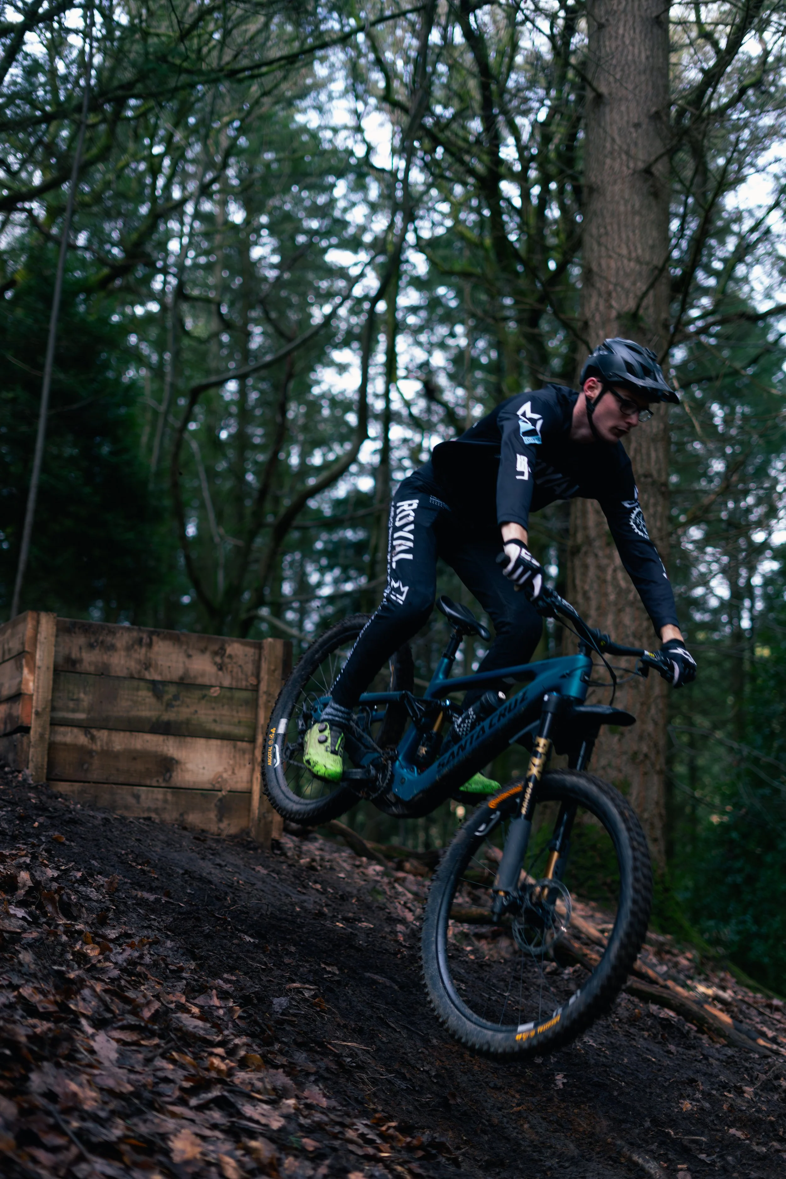 A mountain biker wearing a helmet and black gear riding on a dirt trail in a forested area