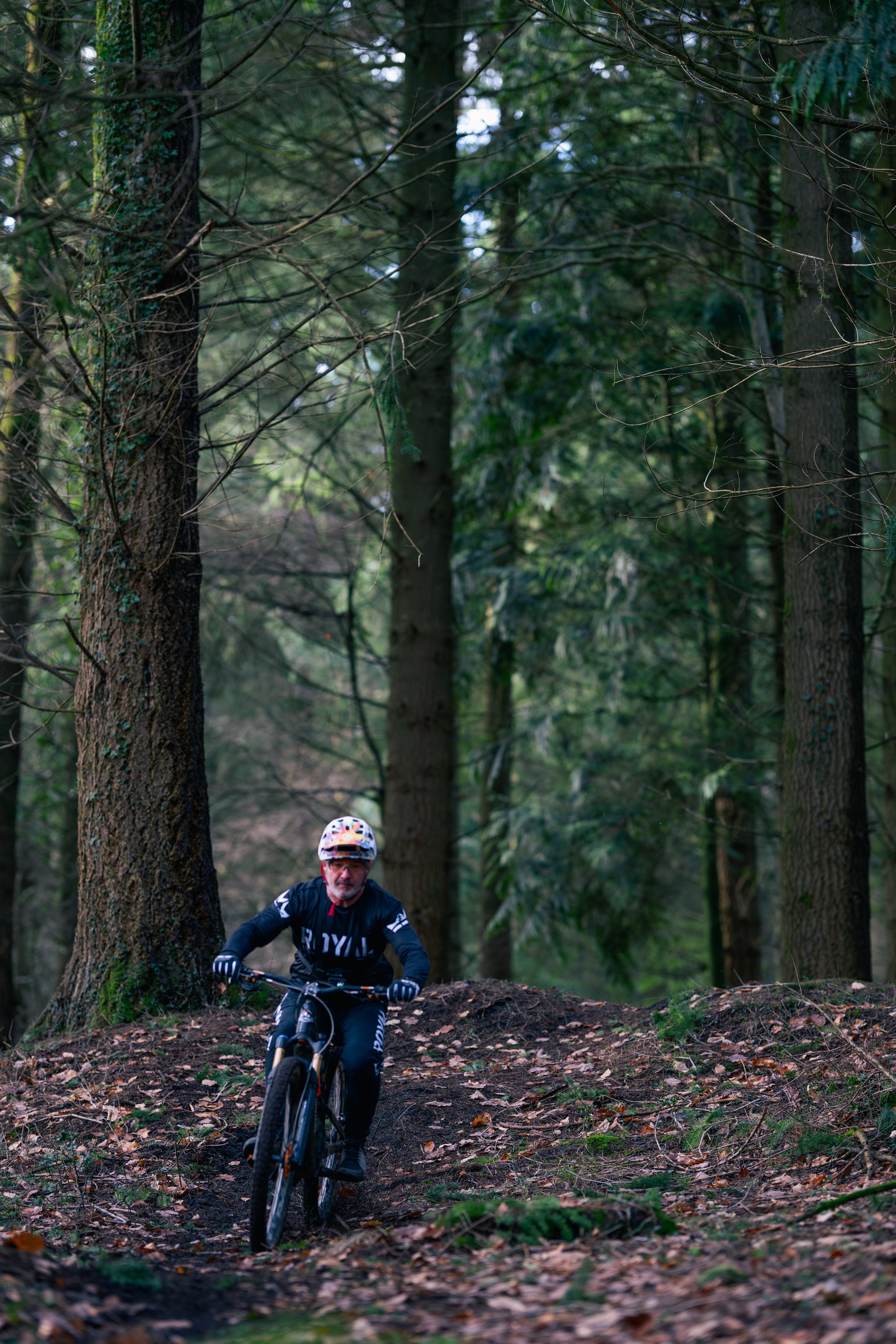 A man mountain biking on a dirt trail through a dense, green forest.