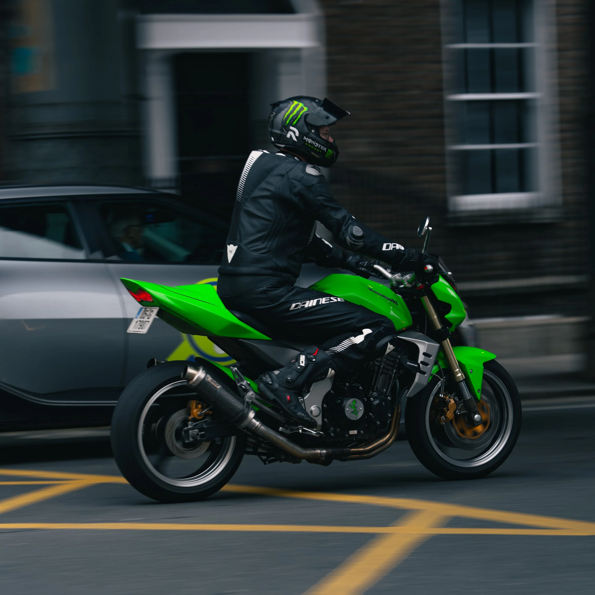 A motorcyclist wearing a black helmet and gear riding a bright green motorcycle on a city street.