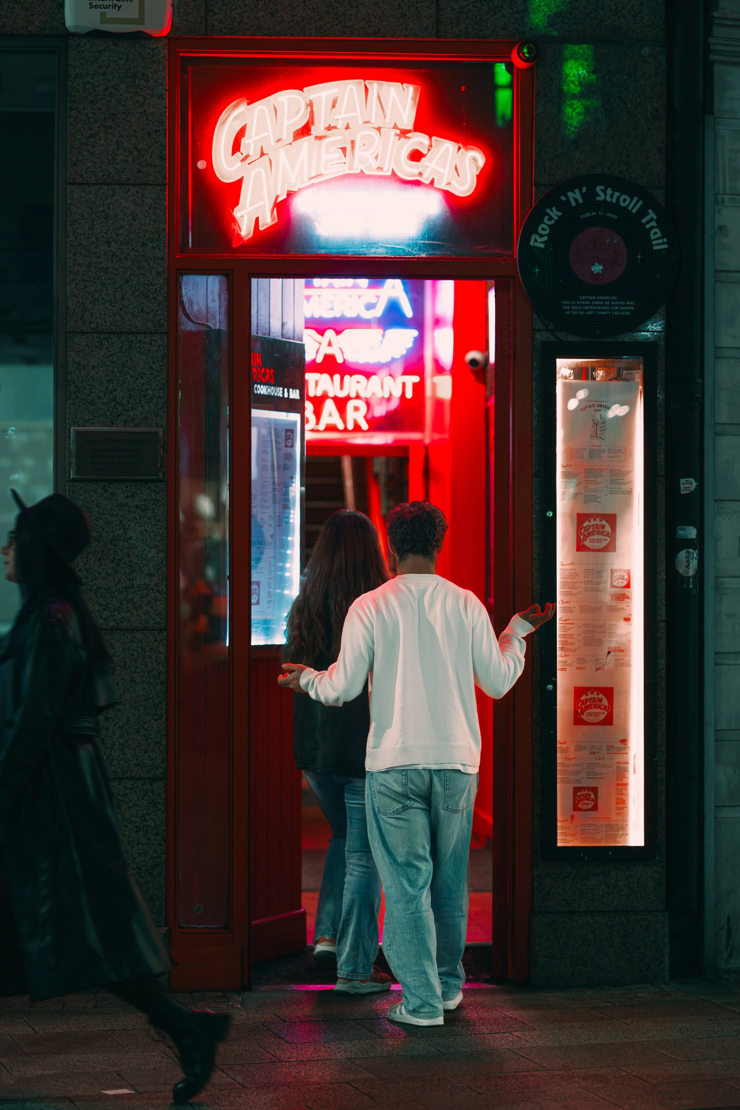 People entering Captain Americans restaurant with neon signs and menu display outside