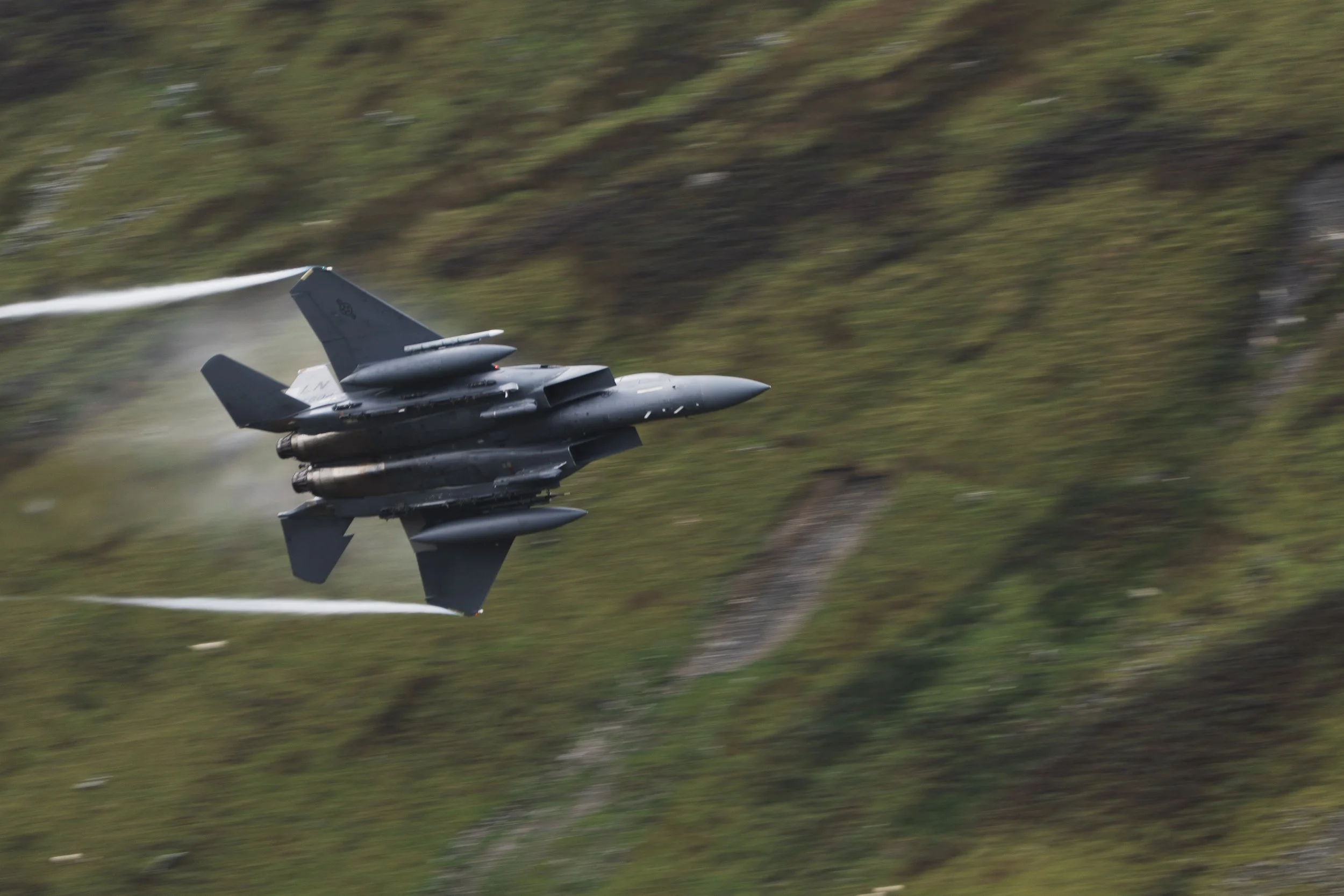 Fighter jet soaring over a grassy hillside with motion blur.
