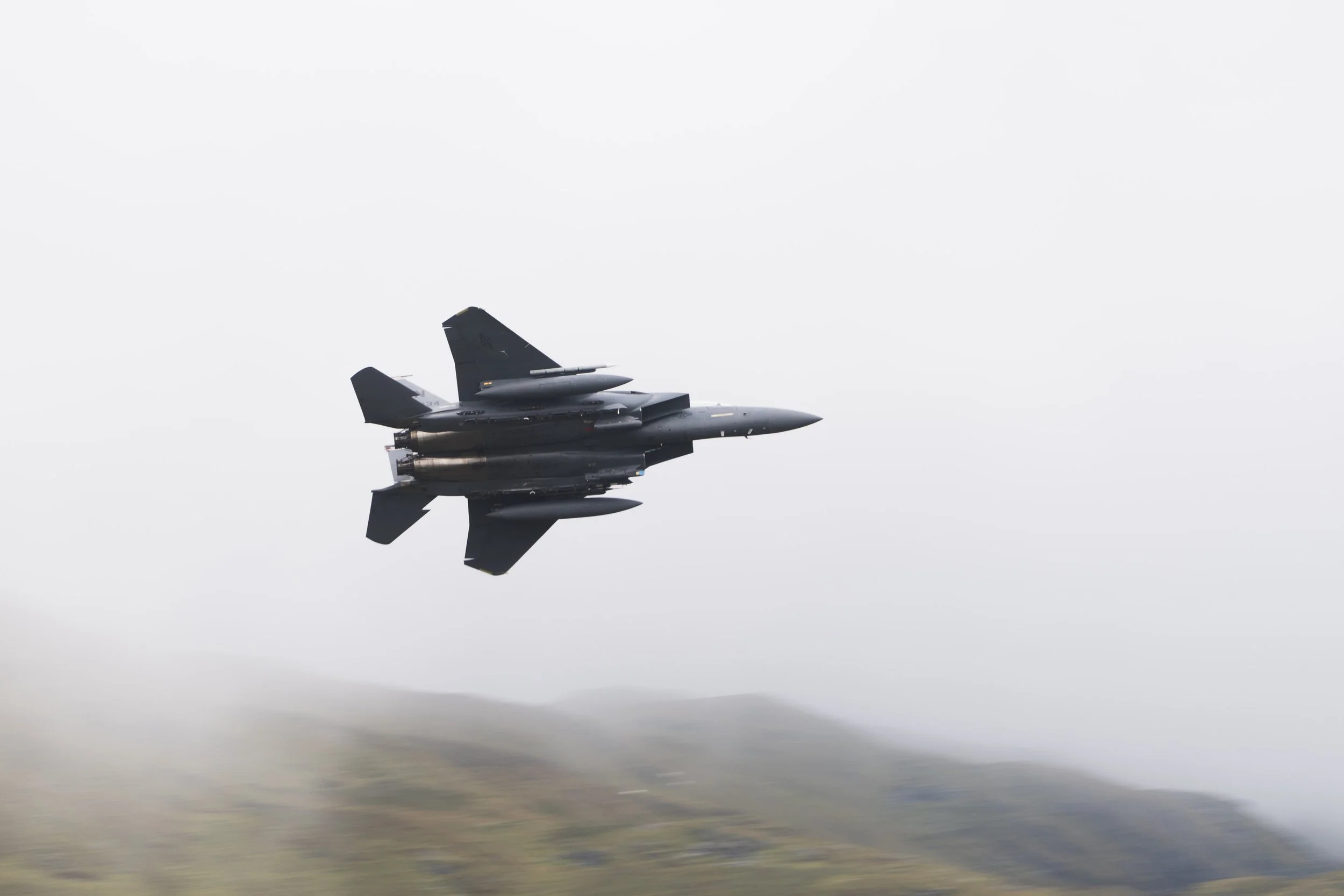 A fighter jet flying in the sky over a blurred landscape.