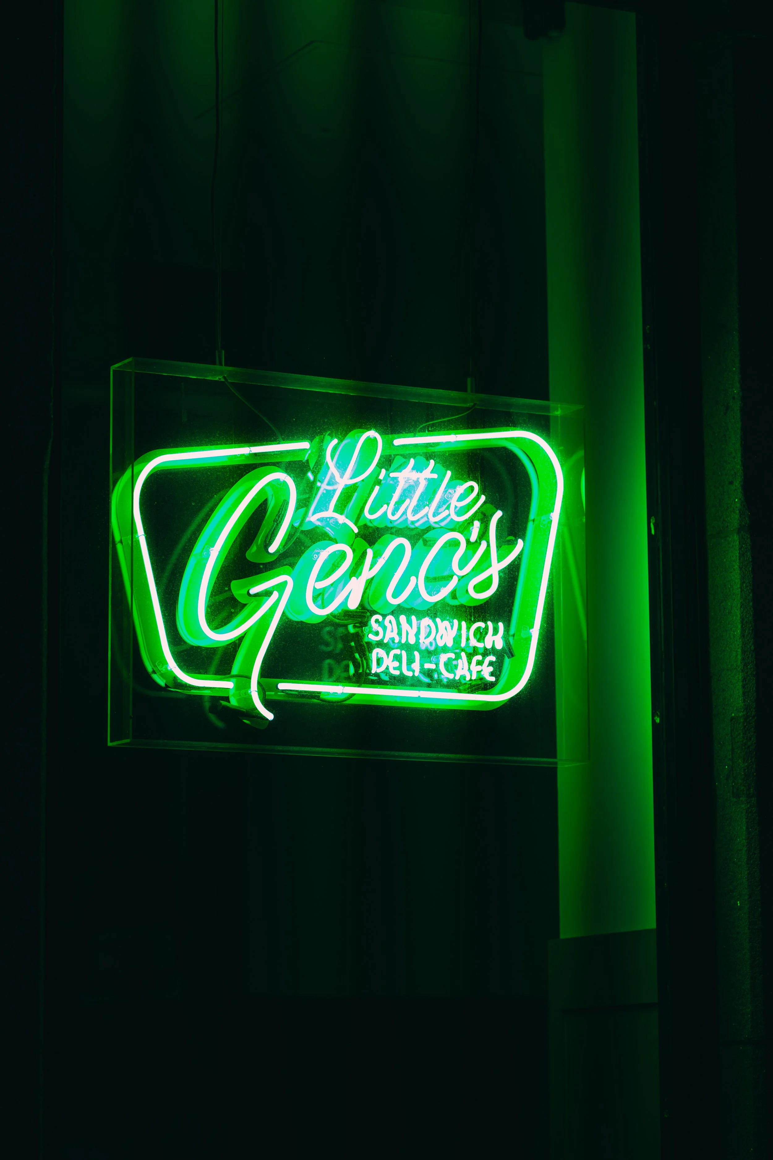 Neon sign for Little Gency's sandwich deli cafe in green and white lights.