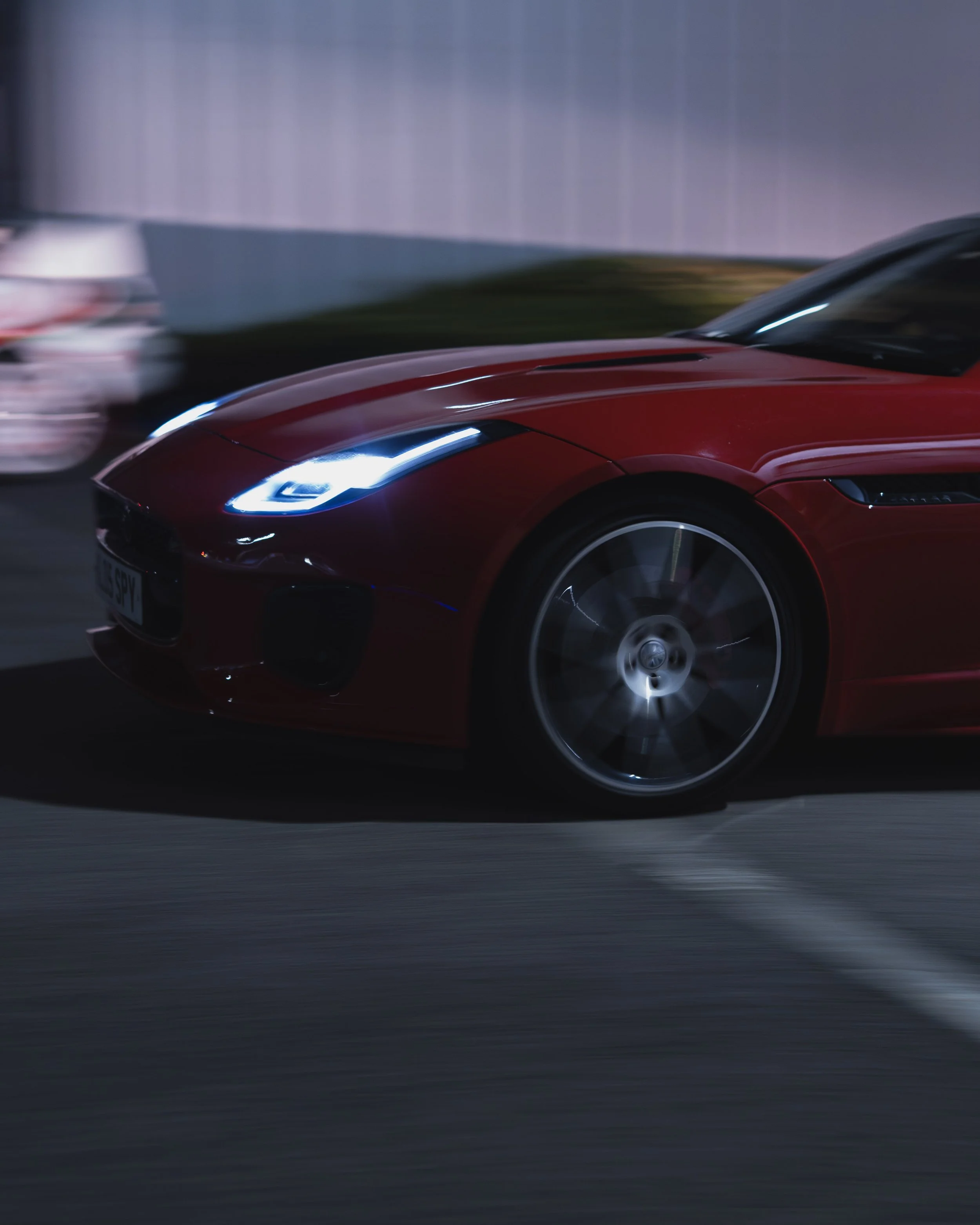 A red jaguar sports car driving at night with headlights on, with another car blurred in the background.