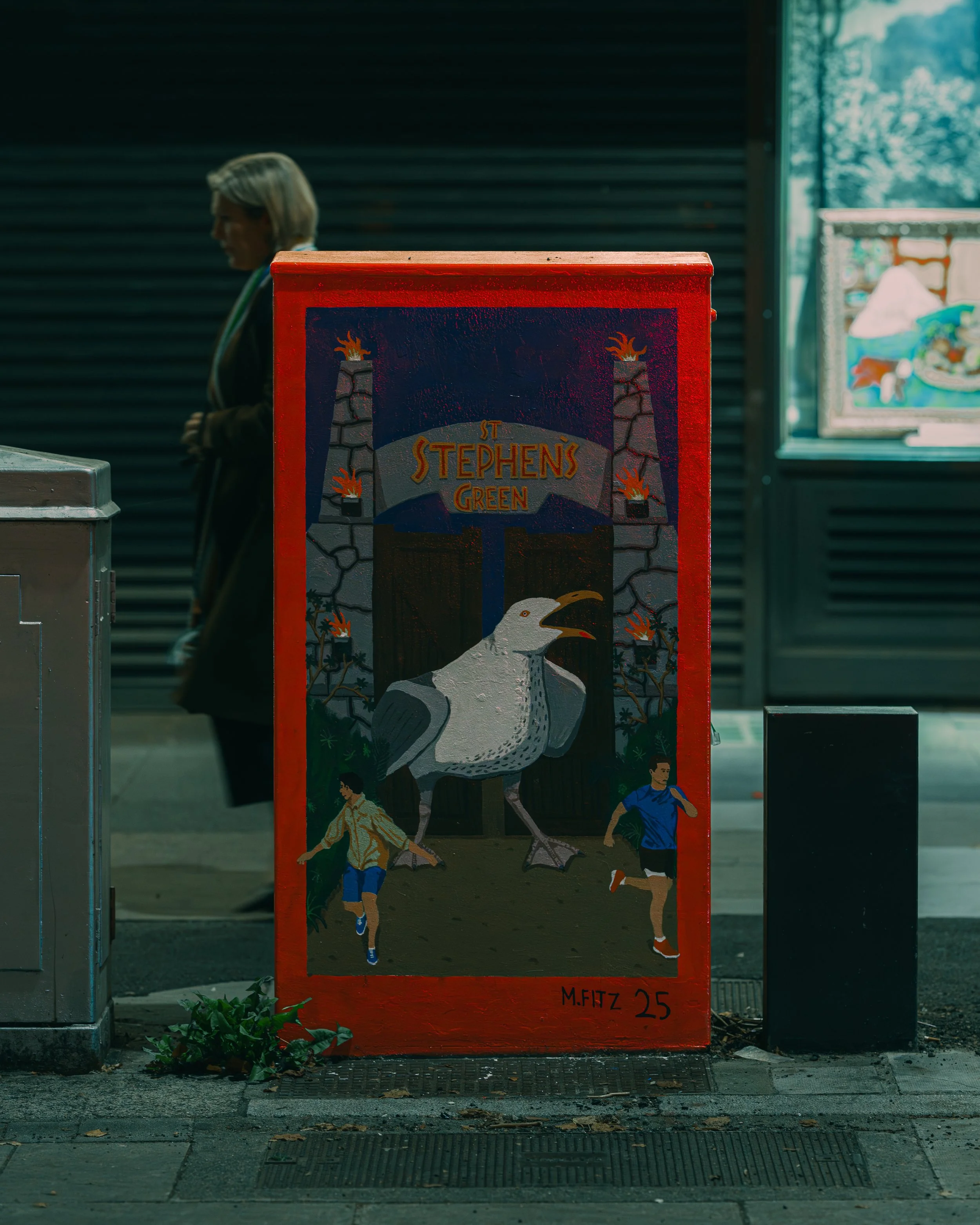 A painted sign for St. Stephen's Green featuring a large seagull and two boys running, with a woman walking in the background, and other artworks visible through a window.