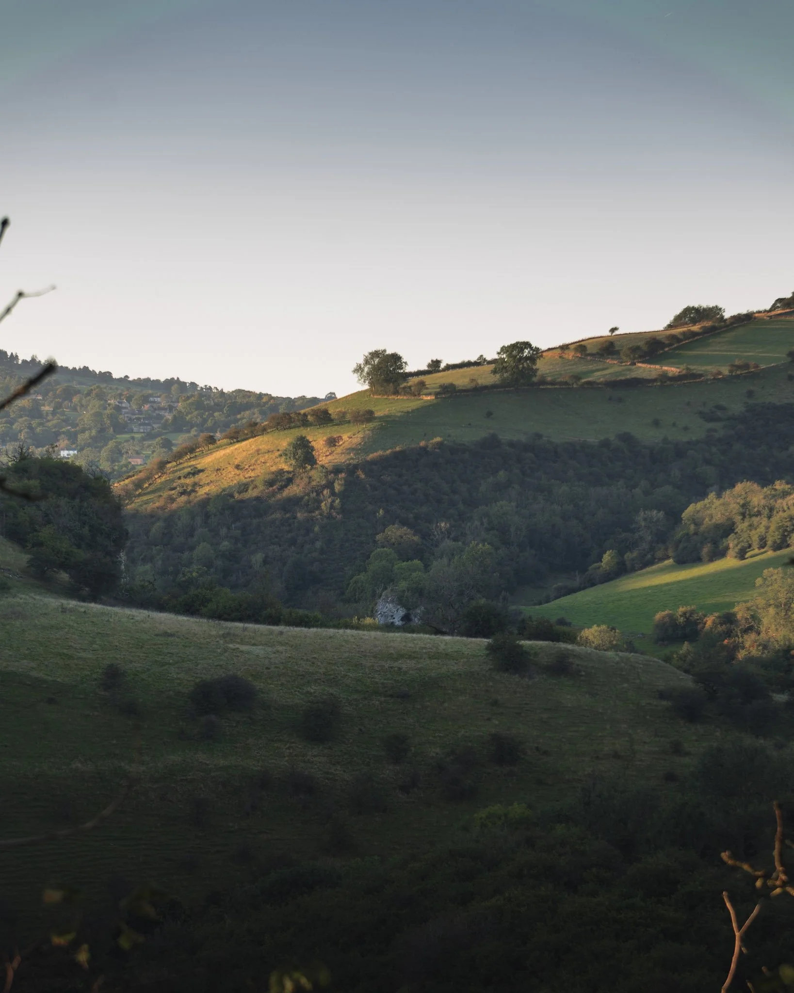 Rolling green hills with trees and patches of sunlight, under a clear sky, the view from thors cave