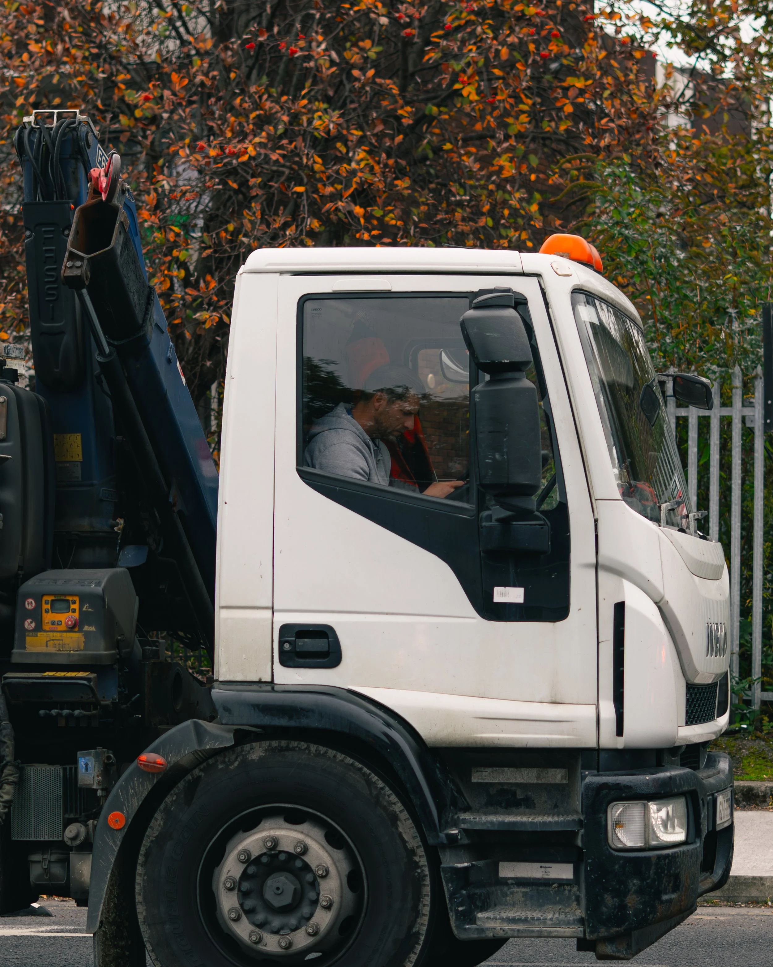 A man sitting inside a white truck with a black side panel, looking at his phone.