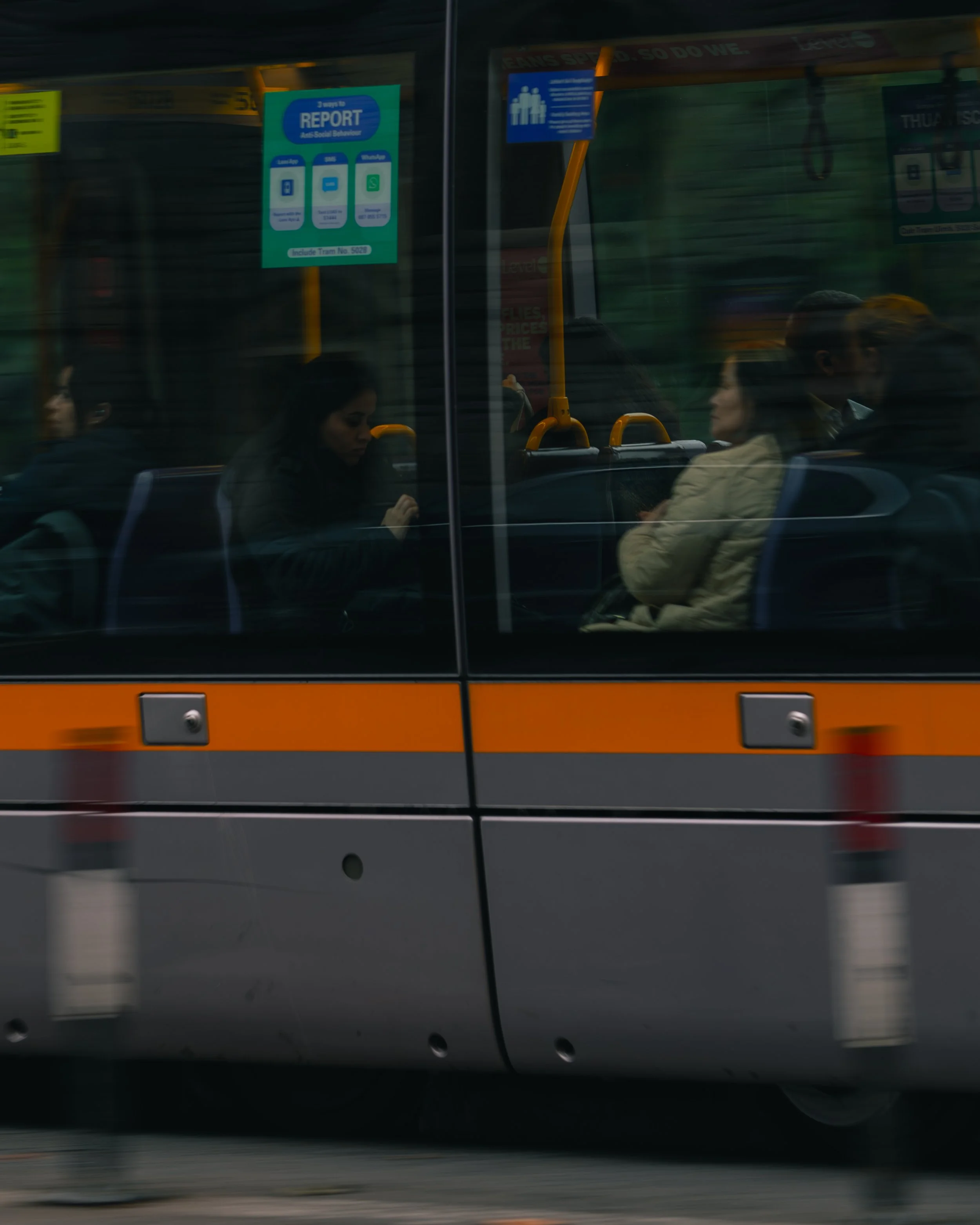 People sitting inside a moving bus, viewed through the window, with social distancing signs and advertisements visible inside.