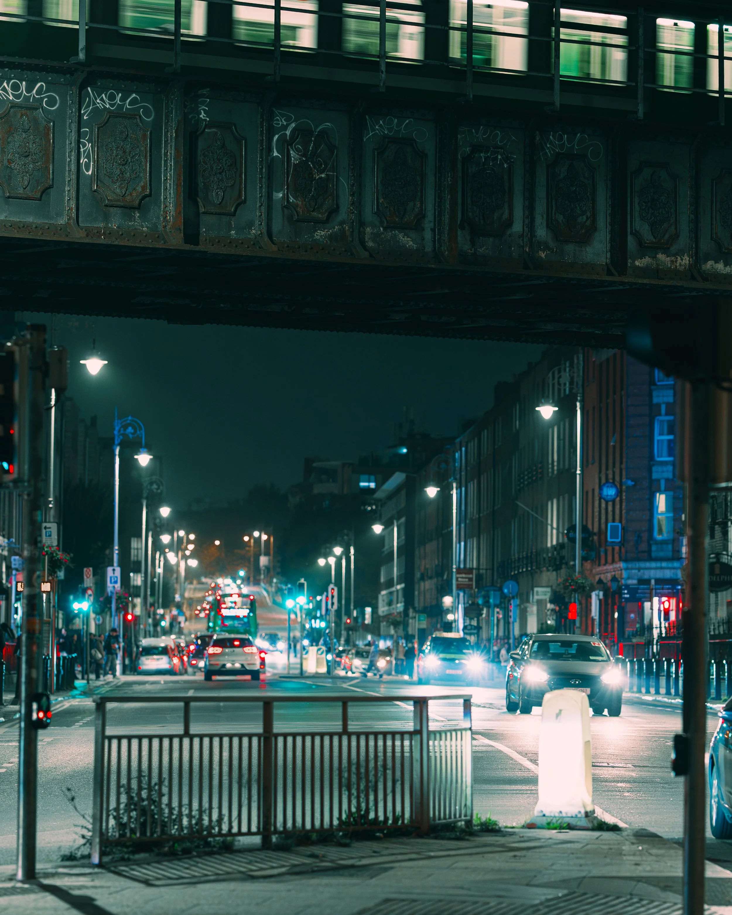 Night urban street scene with moving cars, illuminated streetlights, and a bridge overhead.