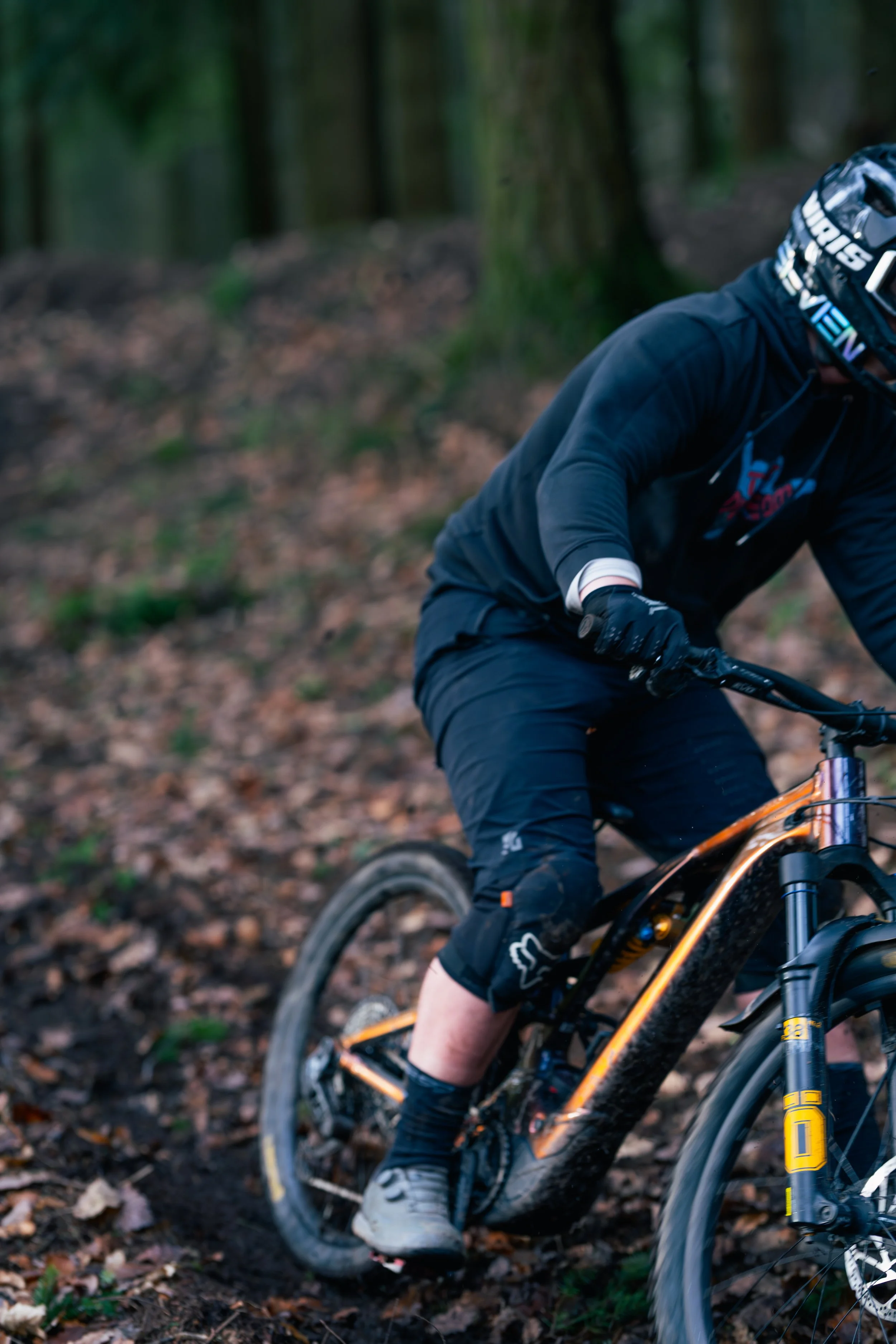 A mountain biker wearing a helmet and protective gear riding on a dirt trail in a wooded forest.