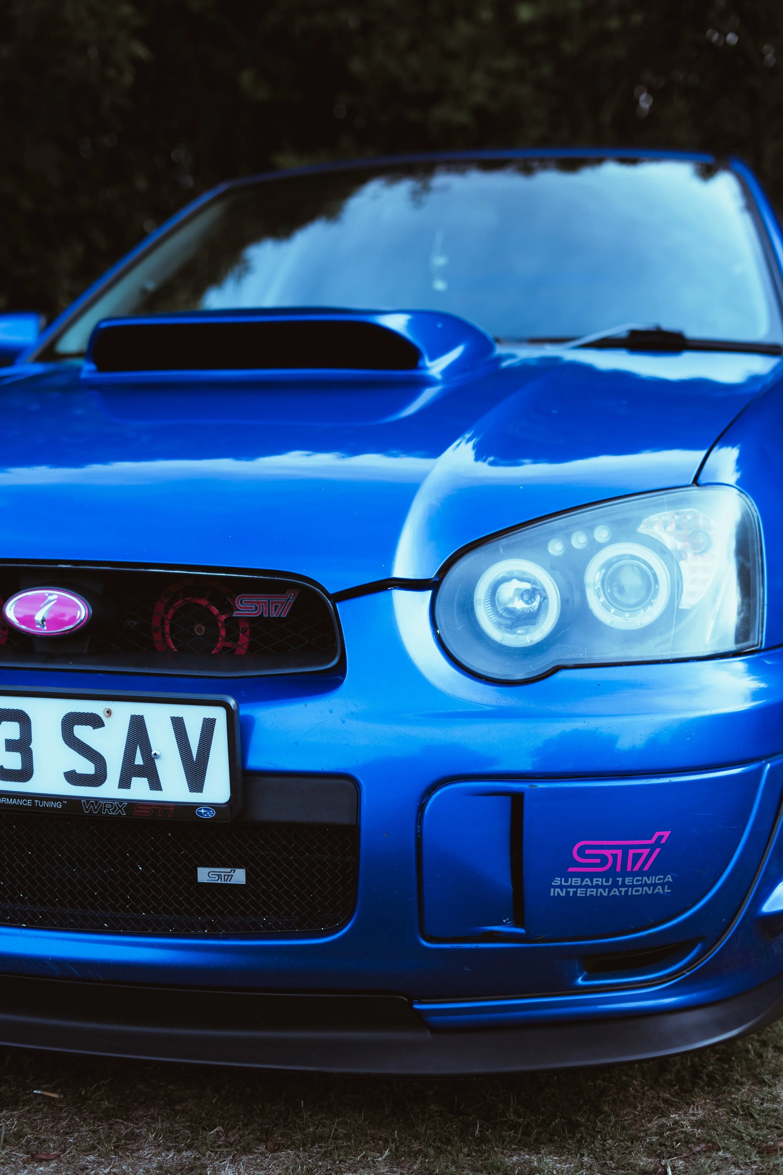 Front view of a blue Subaru Impreza WRX STI with pink Subaru STI decals on the front bumper and grille.