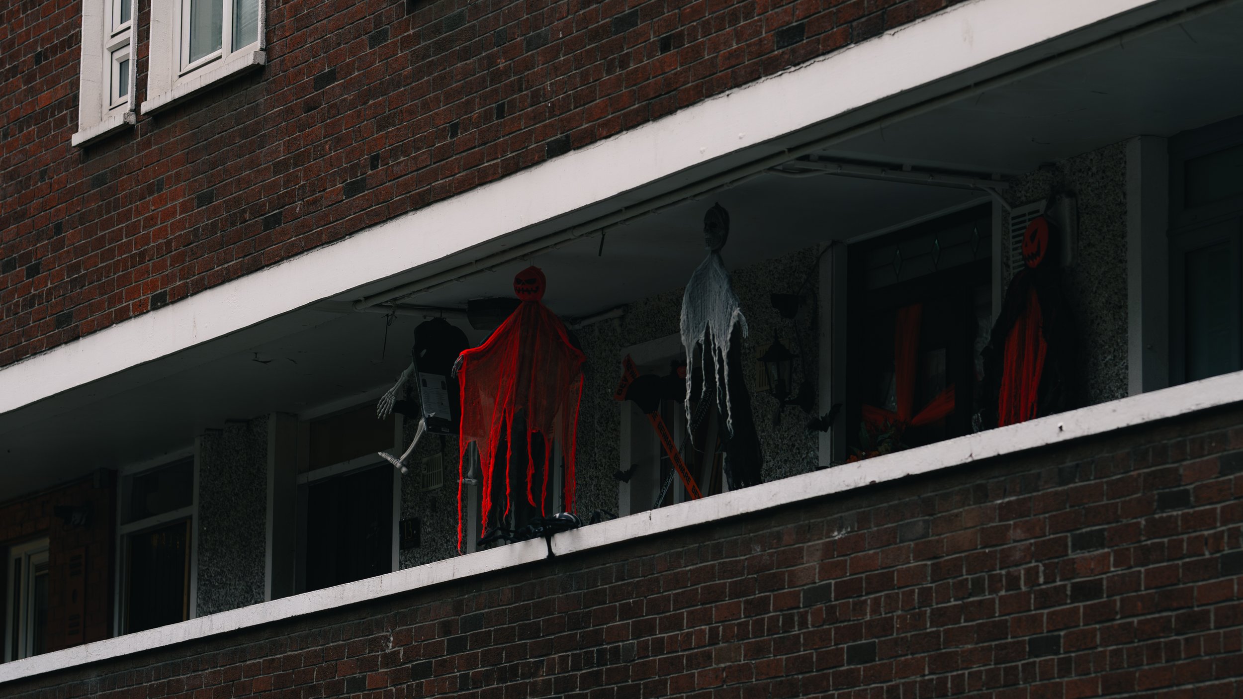 Apartment balcony decorated with Halloween decorations including skeletons and hanging fabric ghosts.