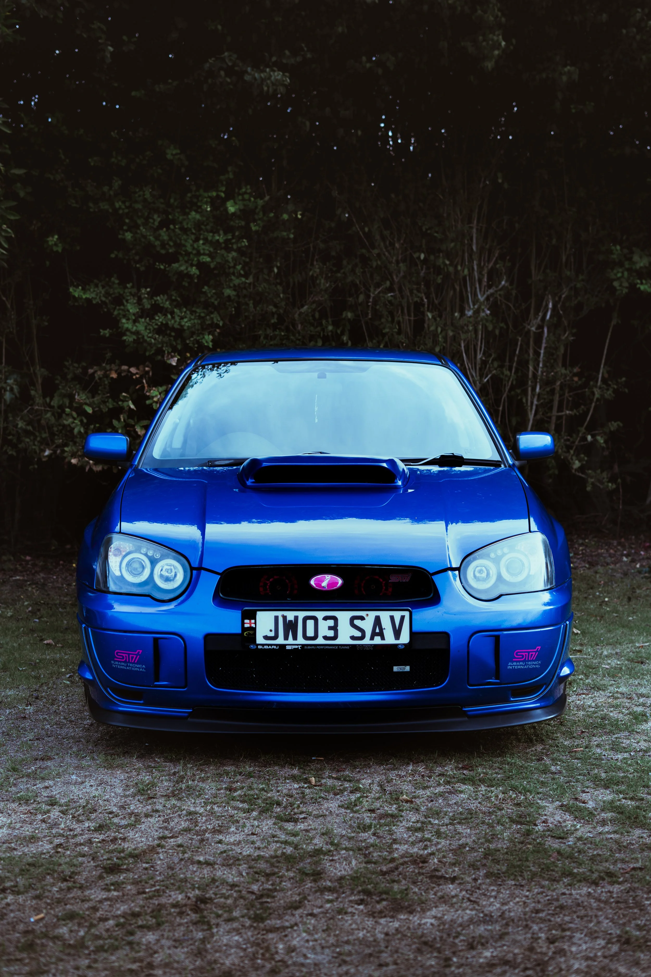 A blue Subaru WRX STI car parked outdoors on a grassy surface with trees in the background.