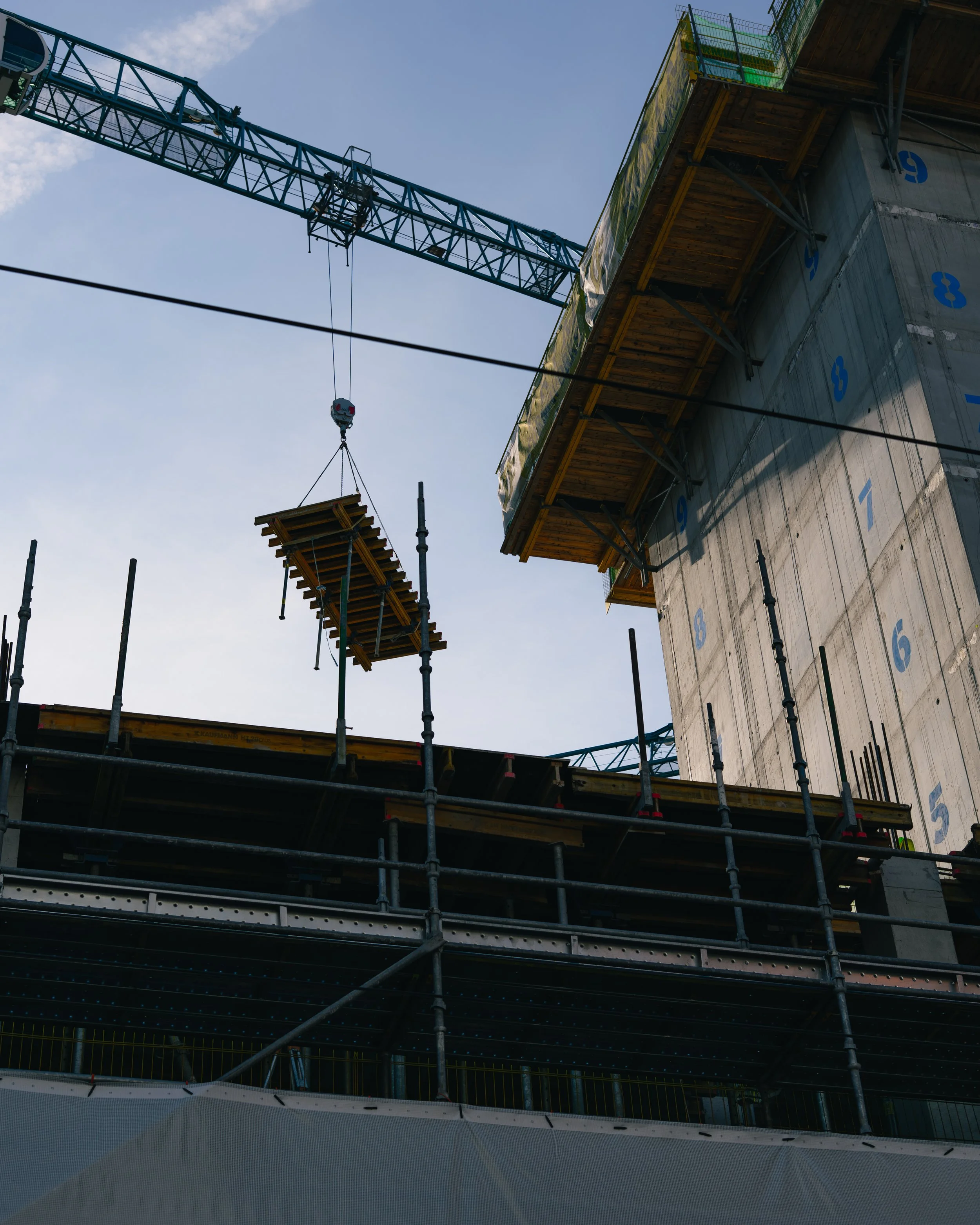 Construction site with scaffolding, a crane hoisting a platform, and a building under construction with numbered concrete sections.