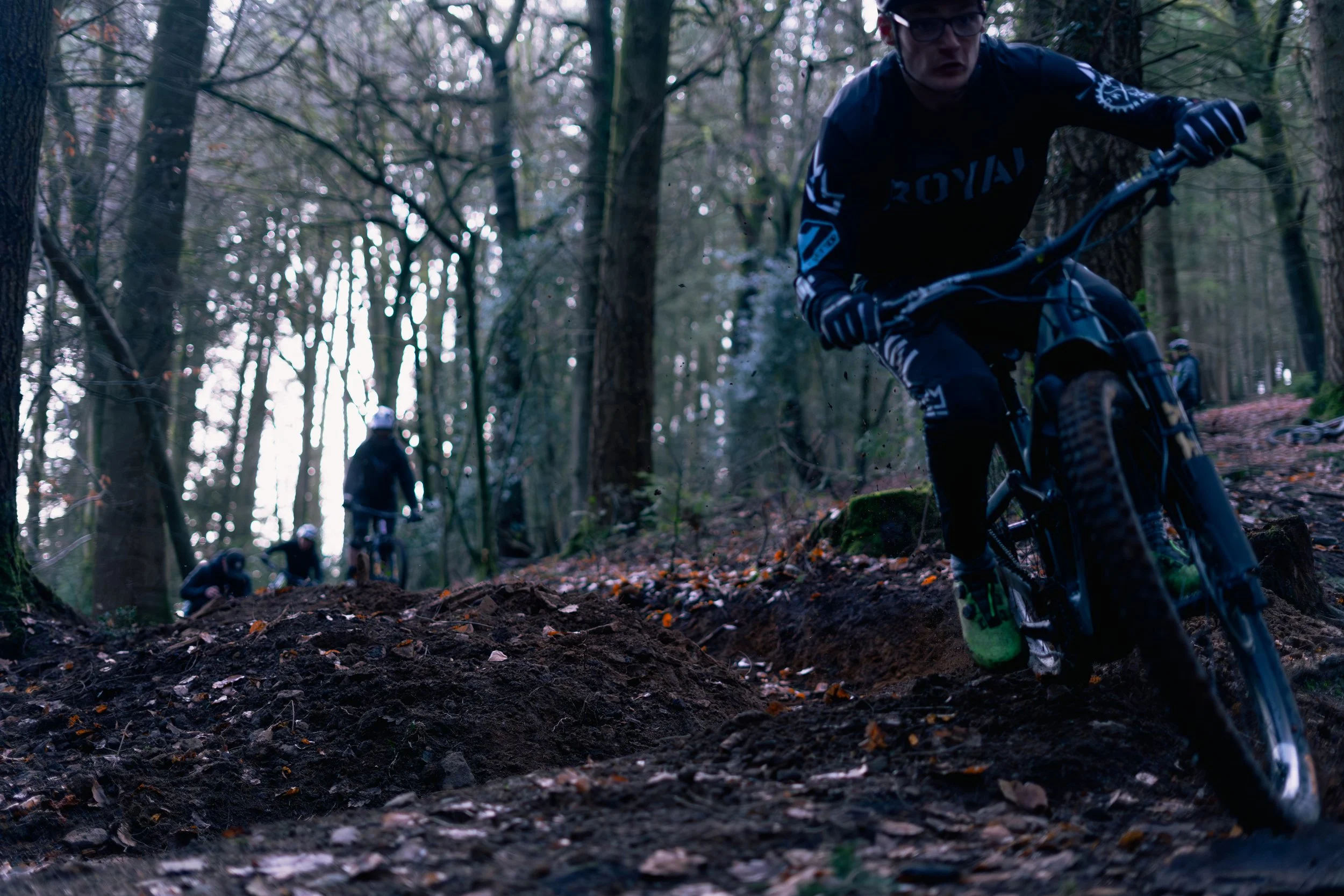 People mountain biking through a wooded trail in a forest.