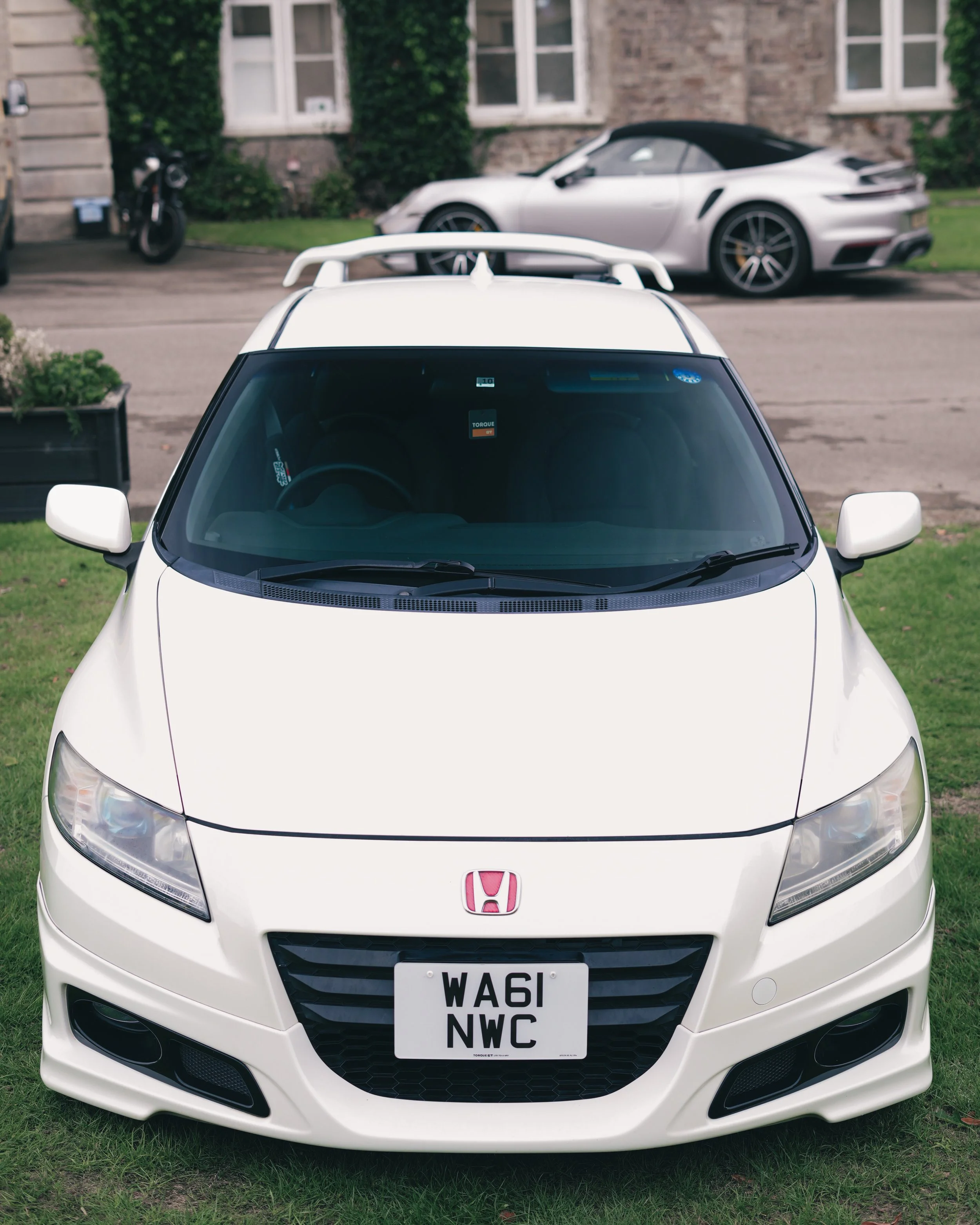 White Honda CR-Z car parked on a grassy area with a silver sports car and a motorcycle in the background.