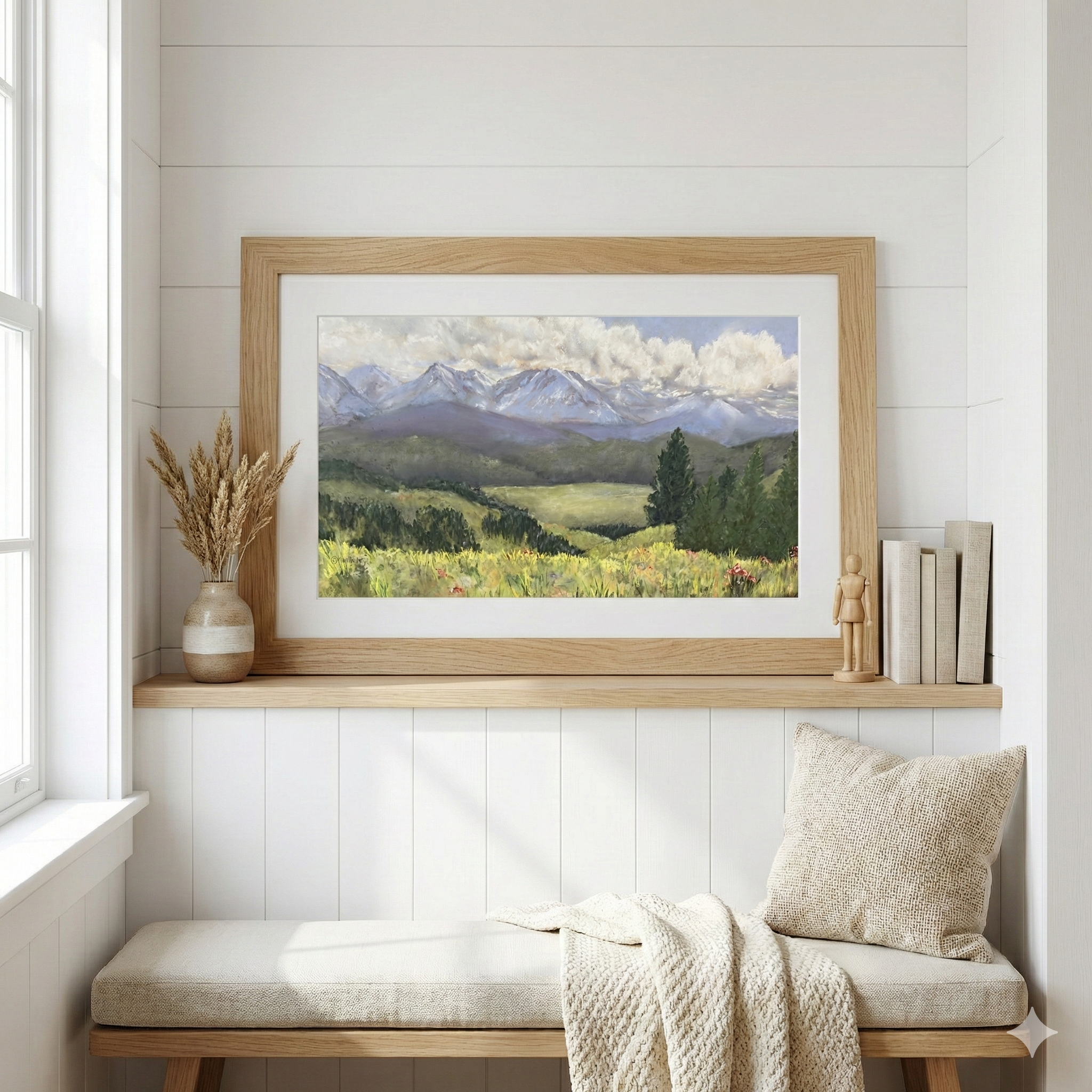 A watercolor painting of mountains, green hills, and a cloudy sky, hung on a white wall in a cozy, decorated room with a bench, a pillow, a blanket, a vase with dried plants, and books.