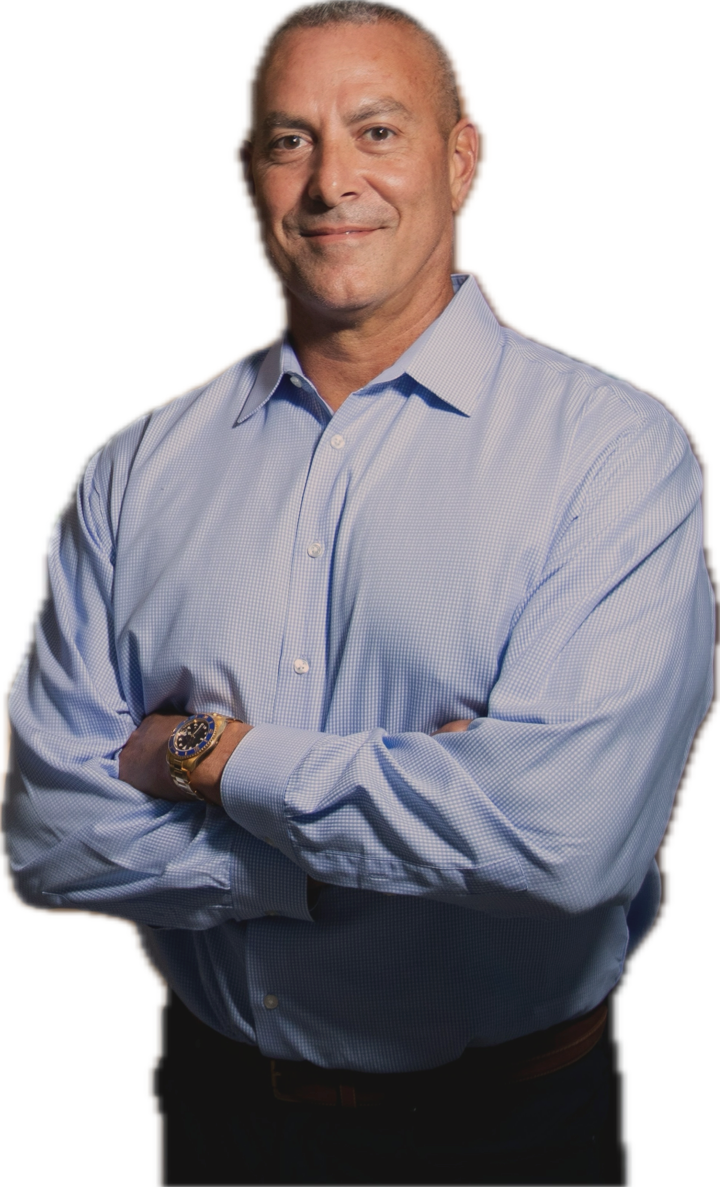 A confident middle-aged man wearing a light blue dress shirt with sleeves rolled up, standing with arms crossed and smiling.