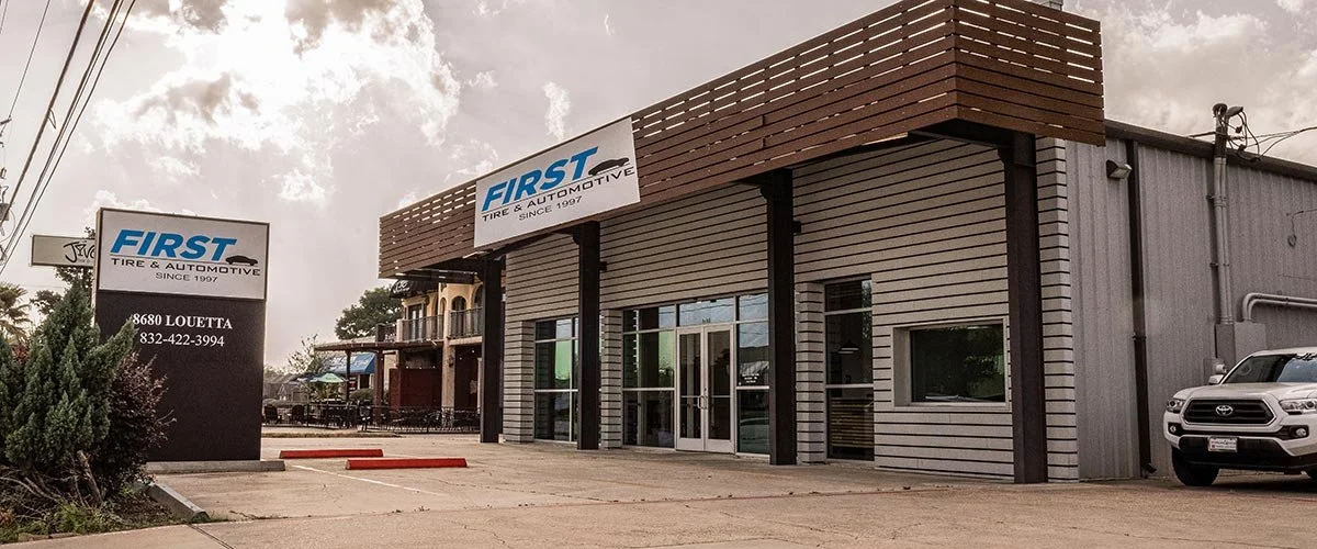 Exterior view of First Tire and Automotive shop, featuring a modern facade with wood and metal accents, and a parked white SUV in front.