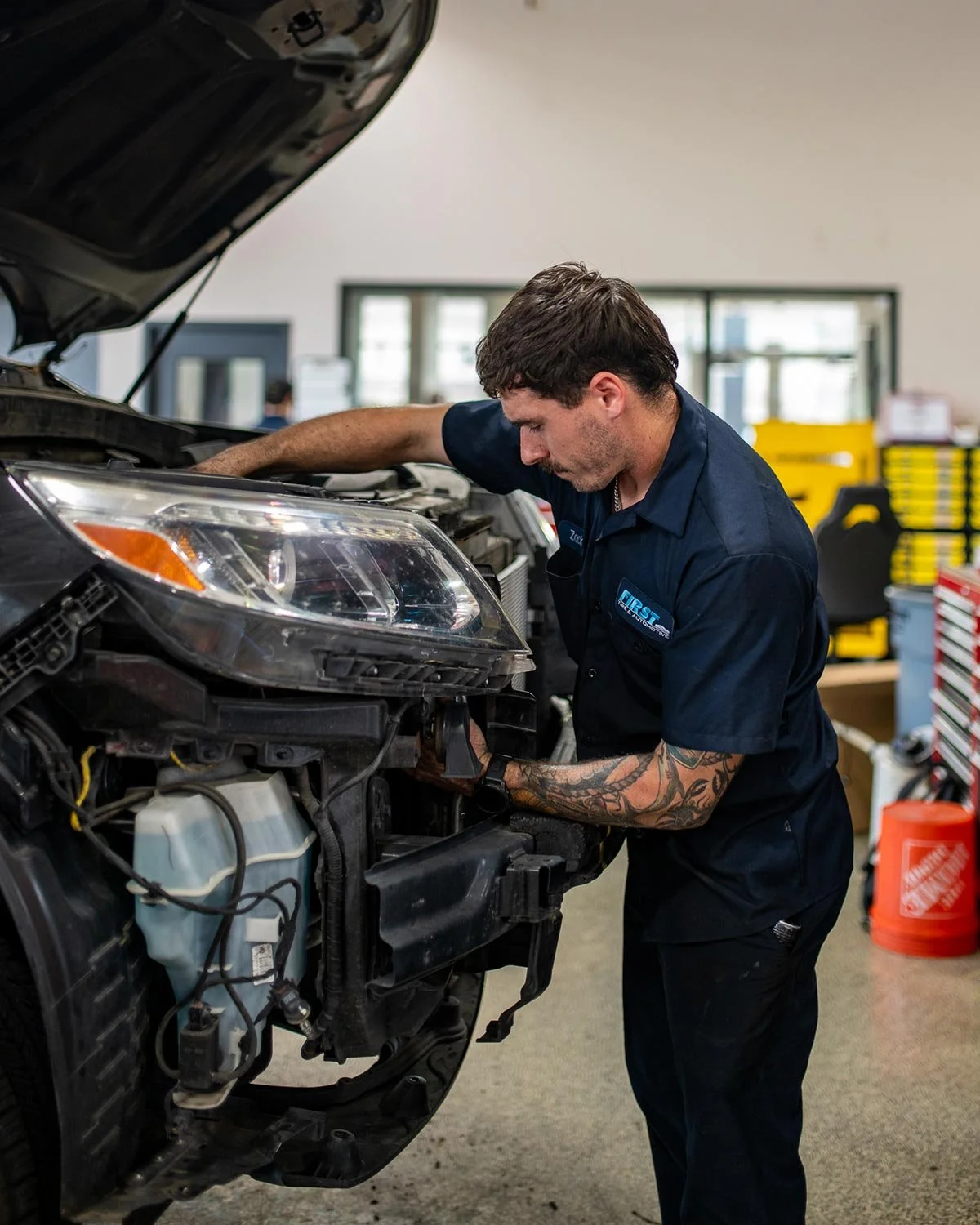 A mechanic working on a car engine inside a repair shop.