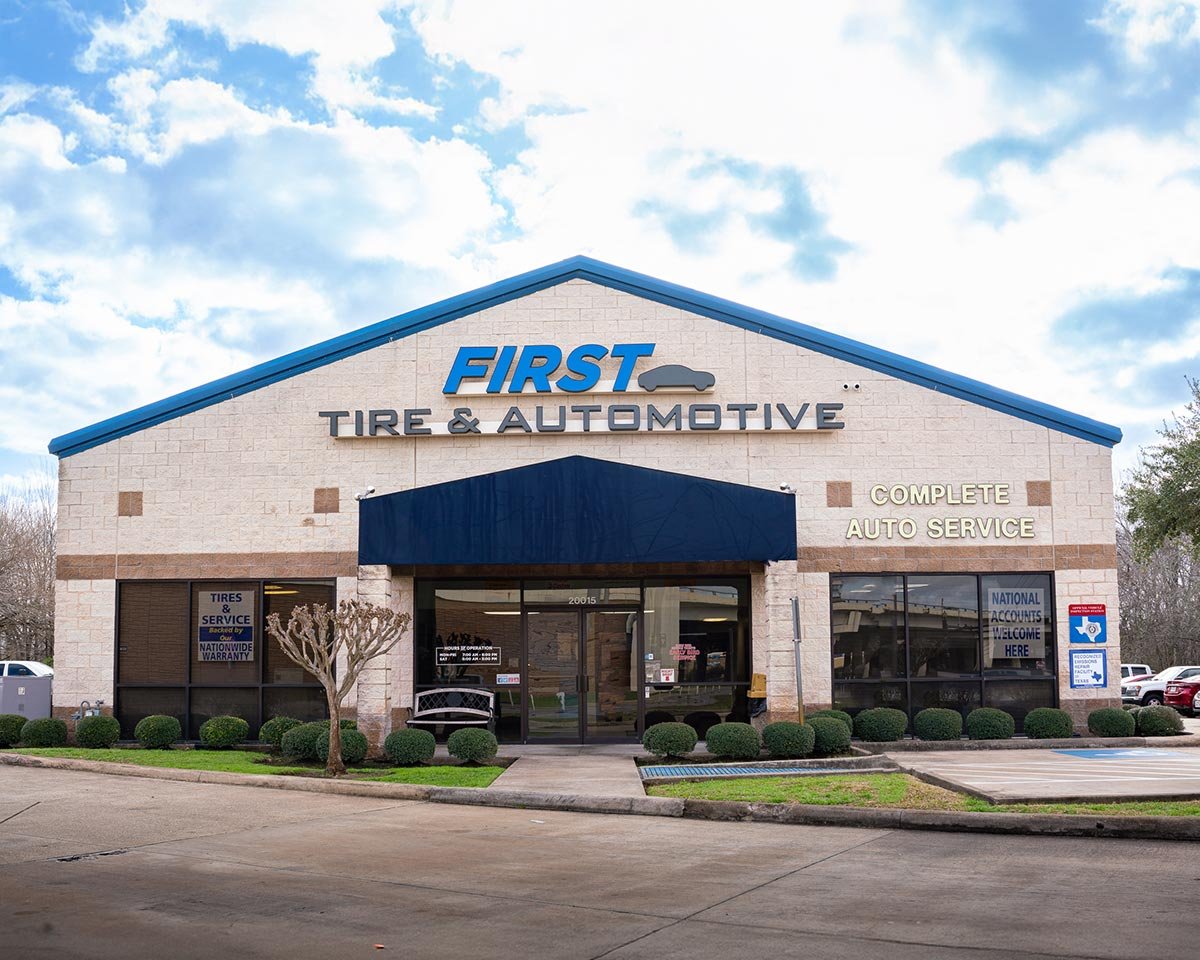 Exterior of First Tire & Automotive shop with a sign indicating complete auto service, a blue awning over the entrance, and parking lot in front.