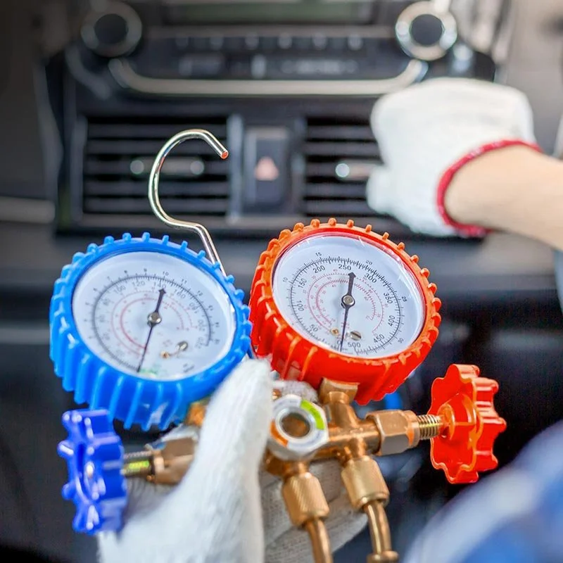 HVAC manifold gauge set with blue and red gauges, connected to a vehicle's air conditioning system for refrigerant pressure testing.