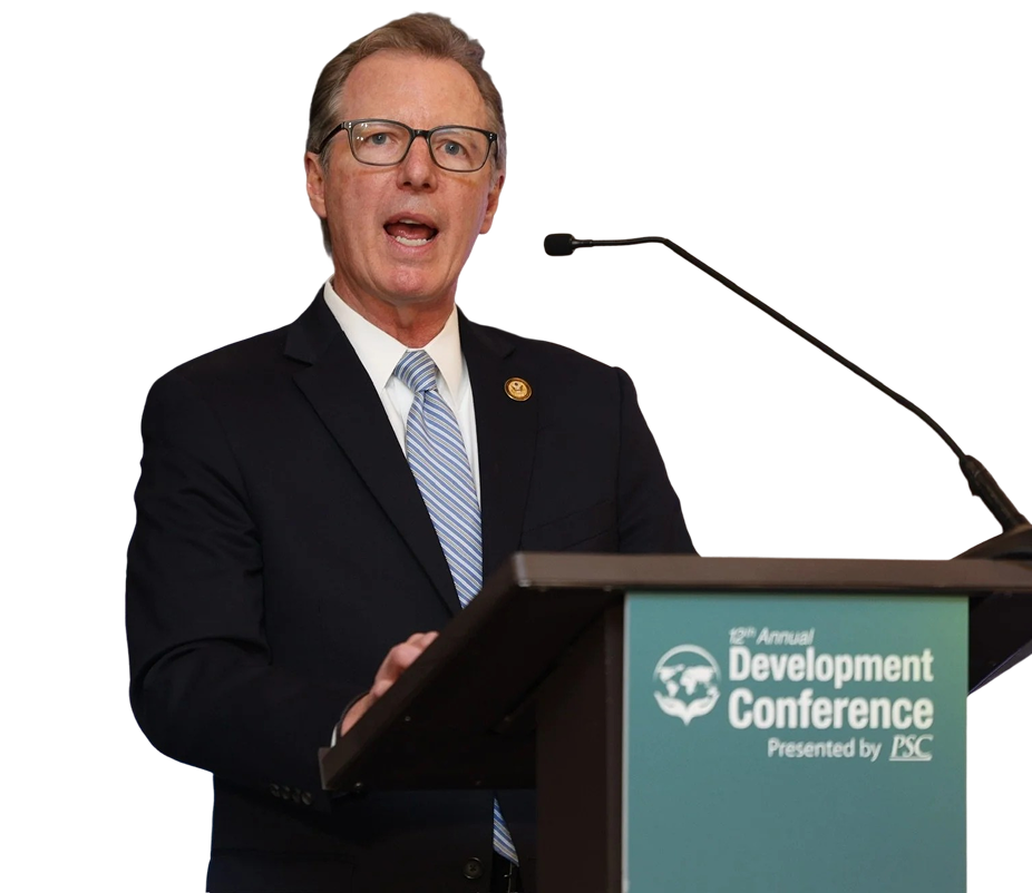 A man wearing glasses and a suit is speaking at a podium during the 12th Annual Development Conference. Paul Martin, former inspector general of USAID and NASA. IGpartners.com co-founder.