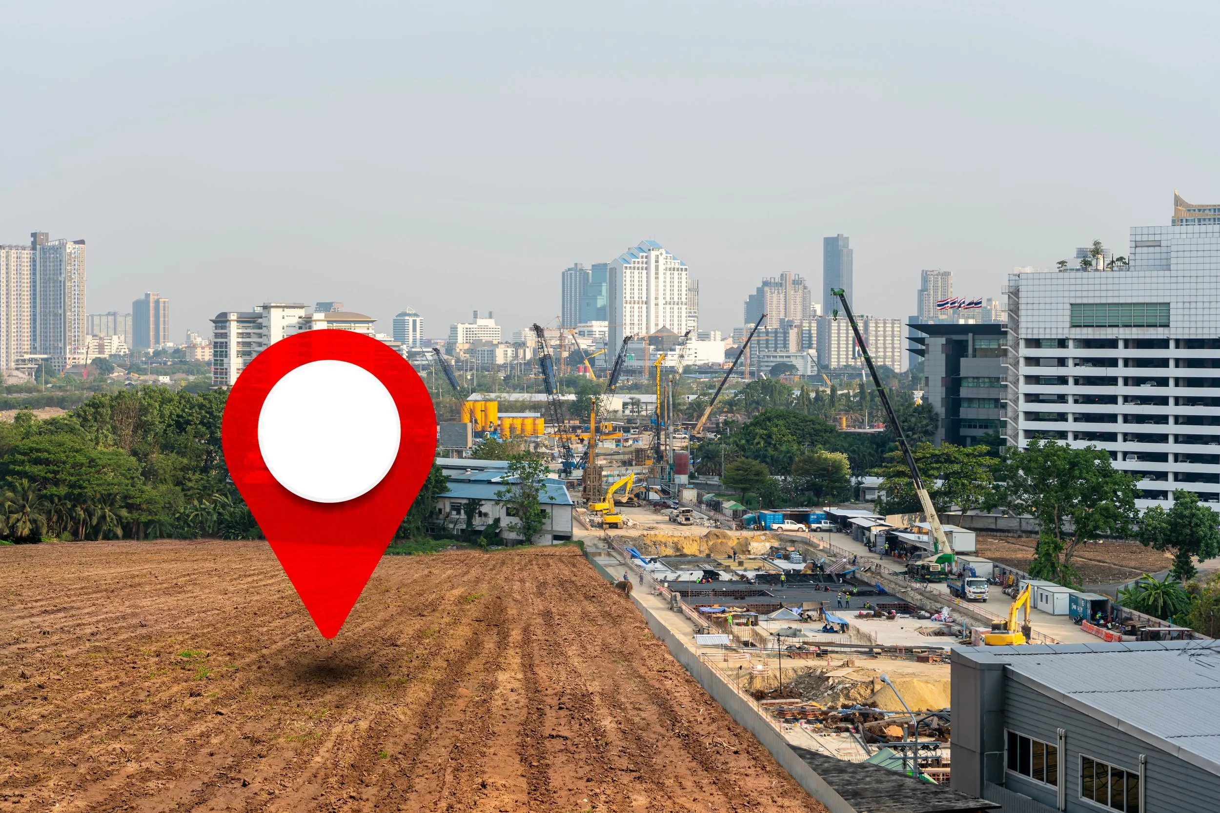 Construction site with cranes and equipment in an urban area, with a city skyline of tall buildings in the background.