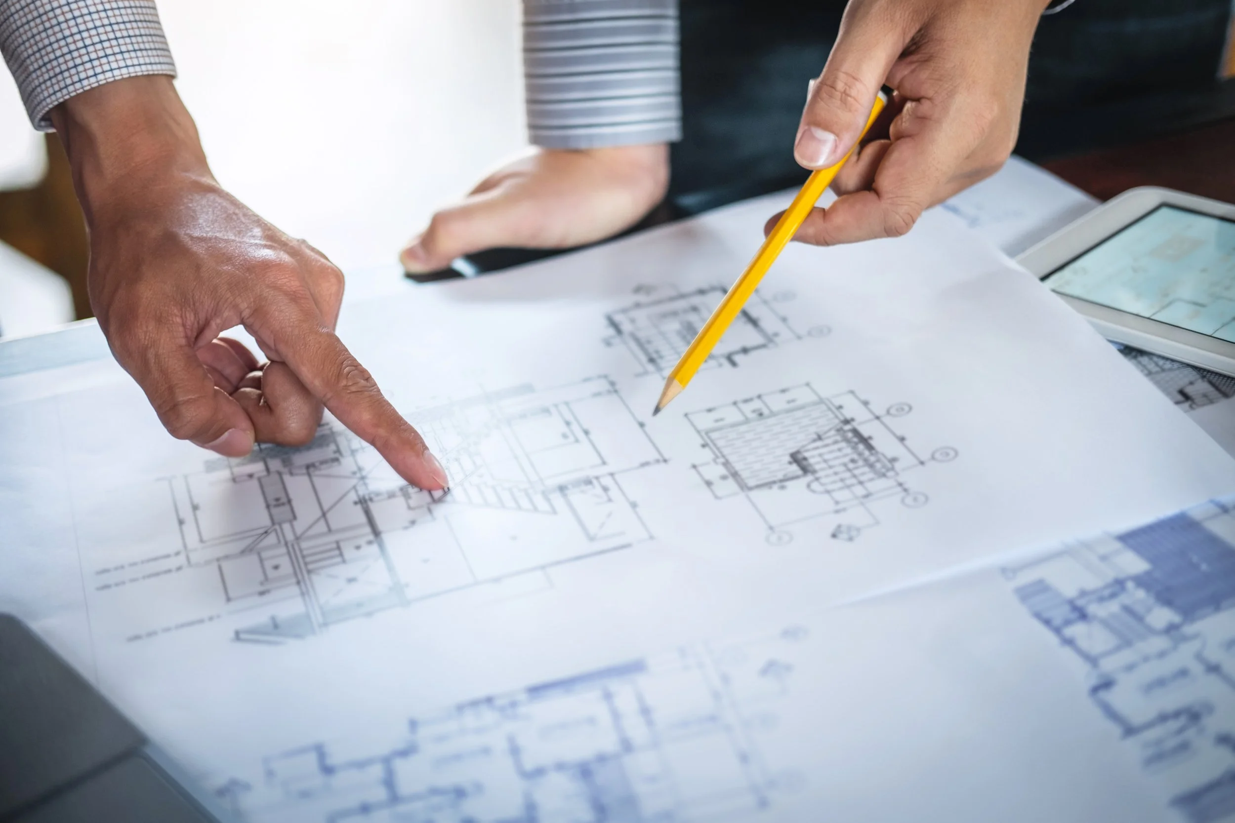 Two people examining architectural blueprints with one person pointing and another holding a yellow pencil.