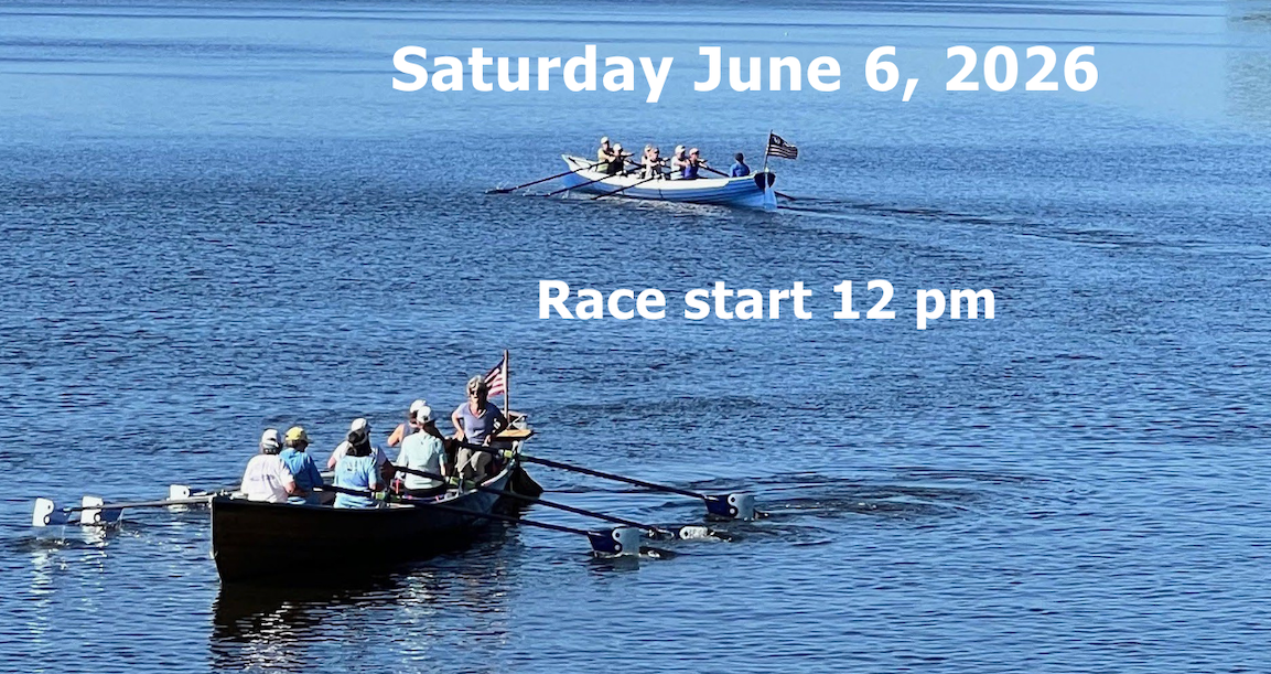 A group of  people in 2 racing boats on a calm body of water with houses and trees on the distant shoreline and an American flag at the stern.