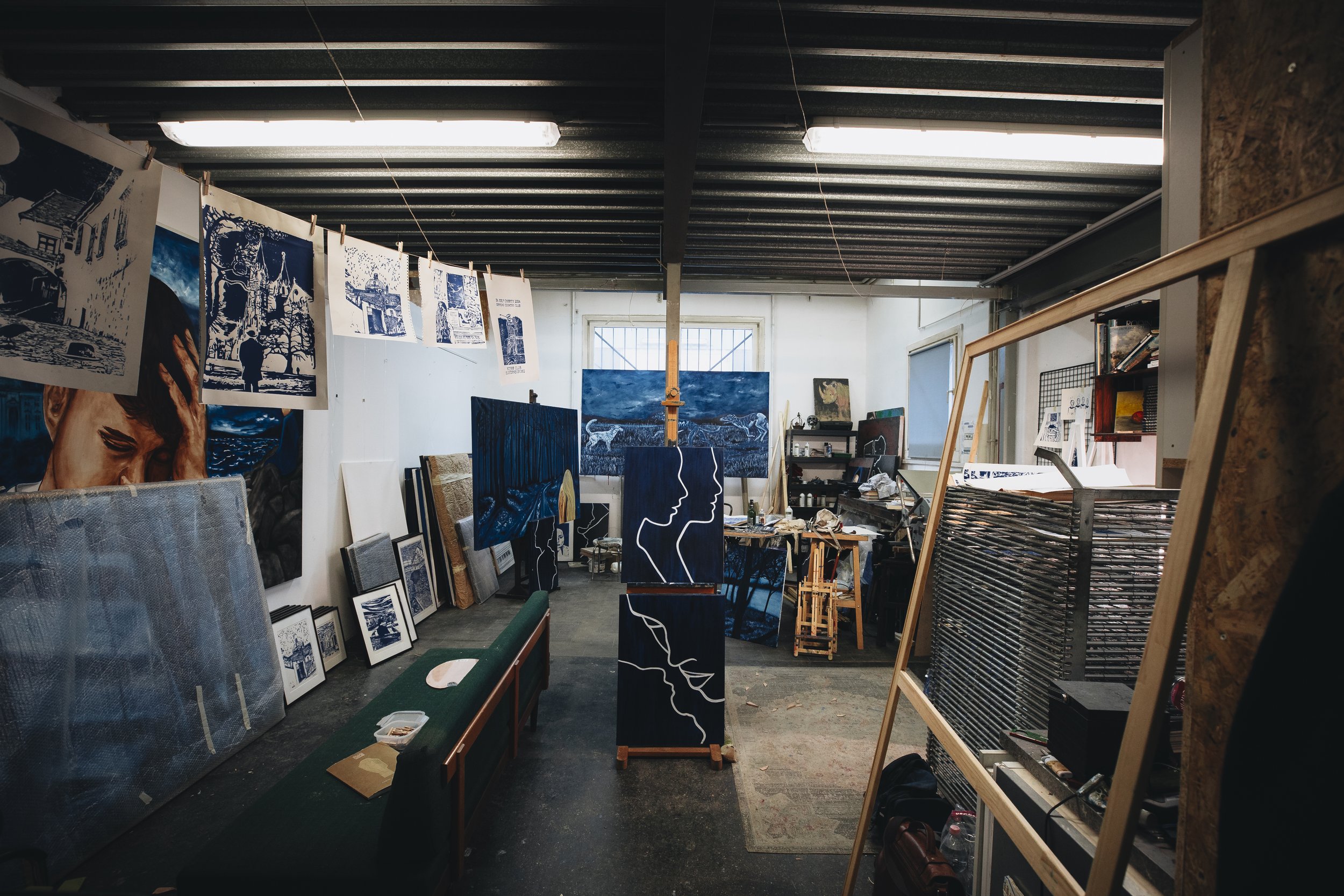 Kunststudio mit zahlreichen Gemälden und Kunstwerken, Leinwänden, Kunstwerken an der Wand und in Arbeit befindlichen Gemälden, viele Bilder hängen an einer Leine, kreative Arbeitsumgebung.