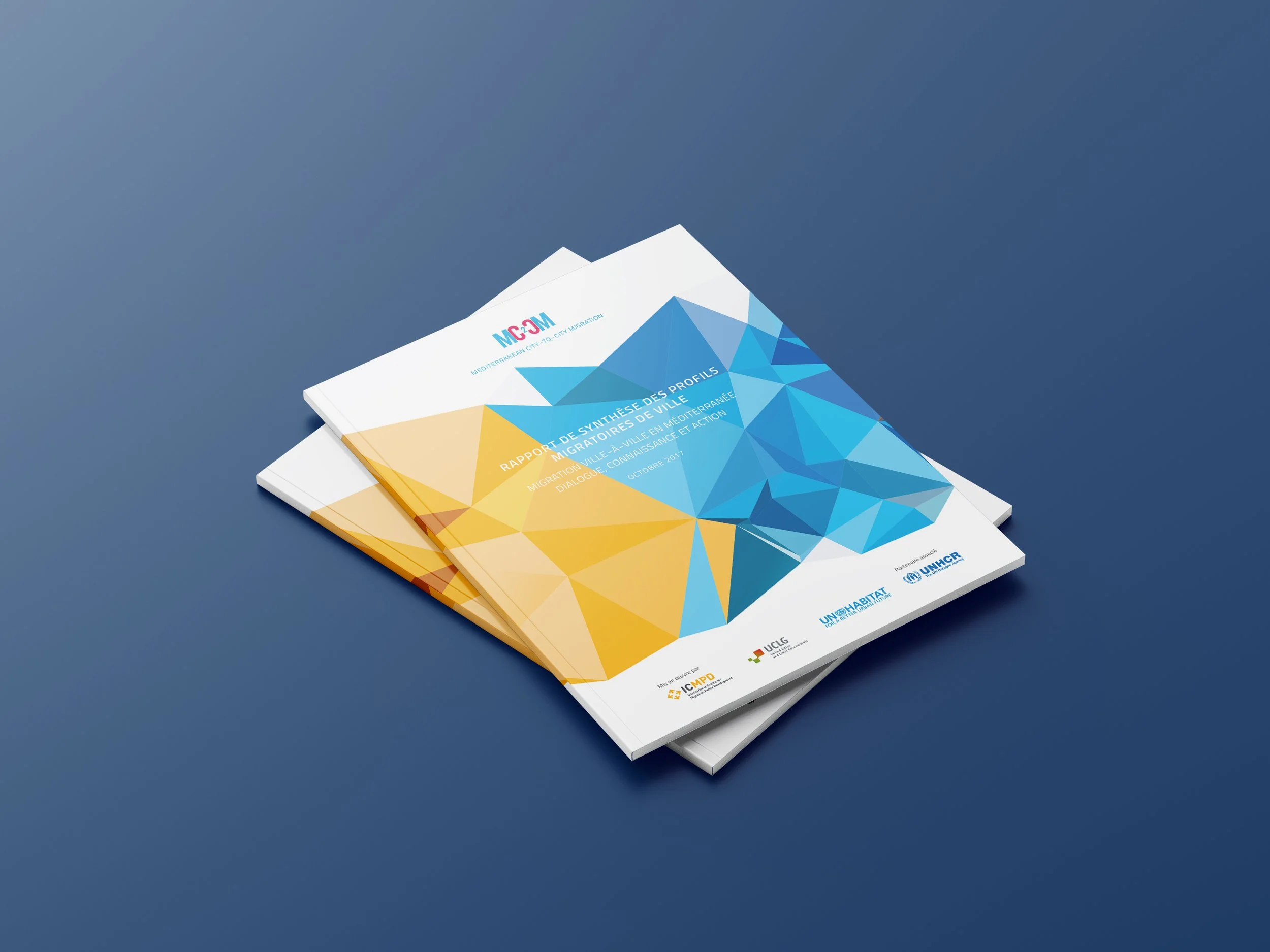 Zwei Broschüren mit geometrischem Design in Blau, Gelb und Orange, auf einem blauen Tisch, die Titel auf Französisch über Migration in mediterranen Städten anzeigen.