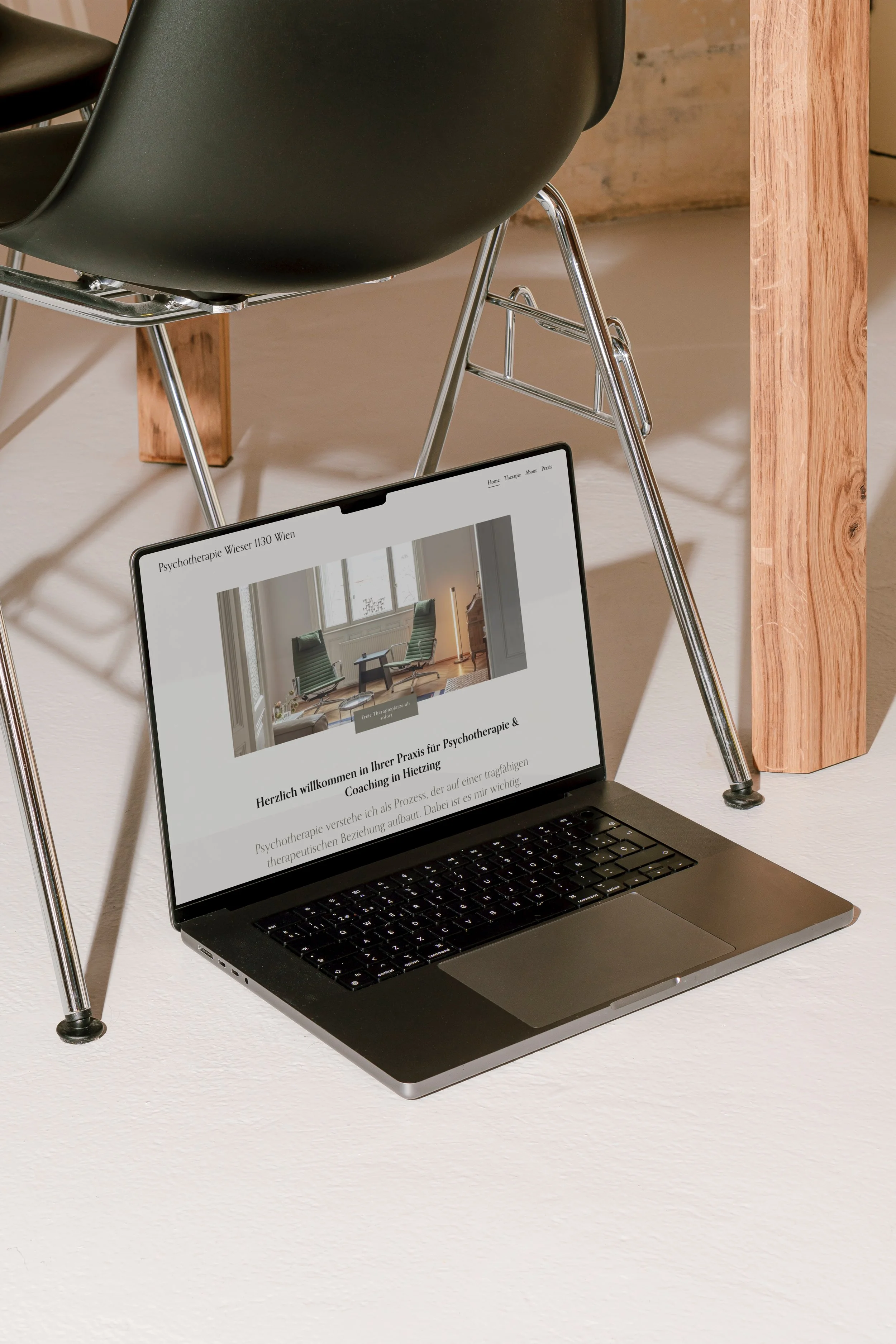 Laptop auf dem Boden, zeigt Webseite für Psychotherapie in Wien, neben einem Stuhl unter einem Tisch.