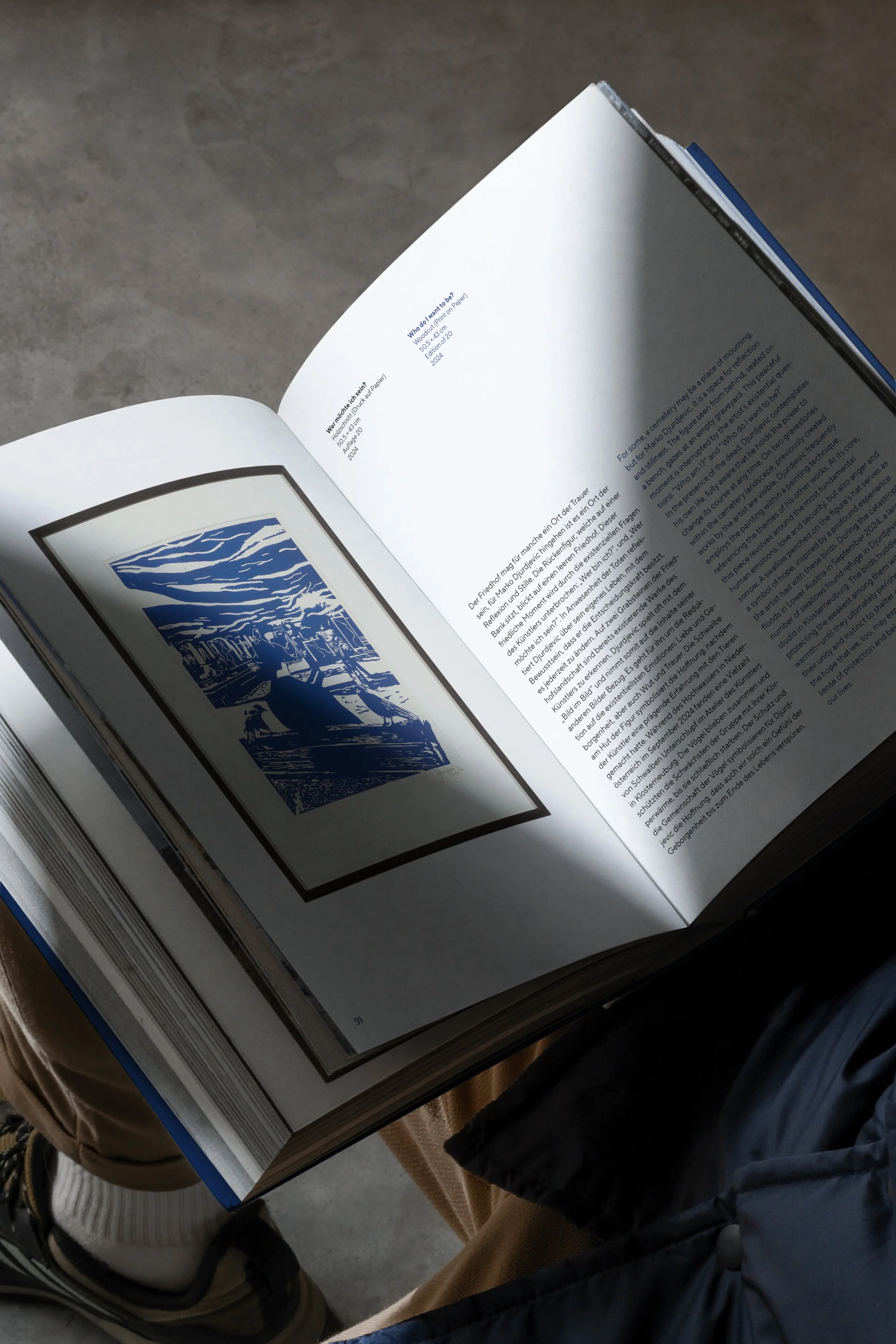 Offenbares Buch mit einem schwarz-weißen Bild auf der linken Seite und deutschen Text auf der rechten Seite, auf einem grauen Boden liegend.