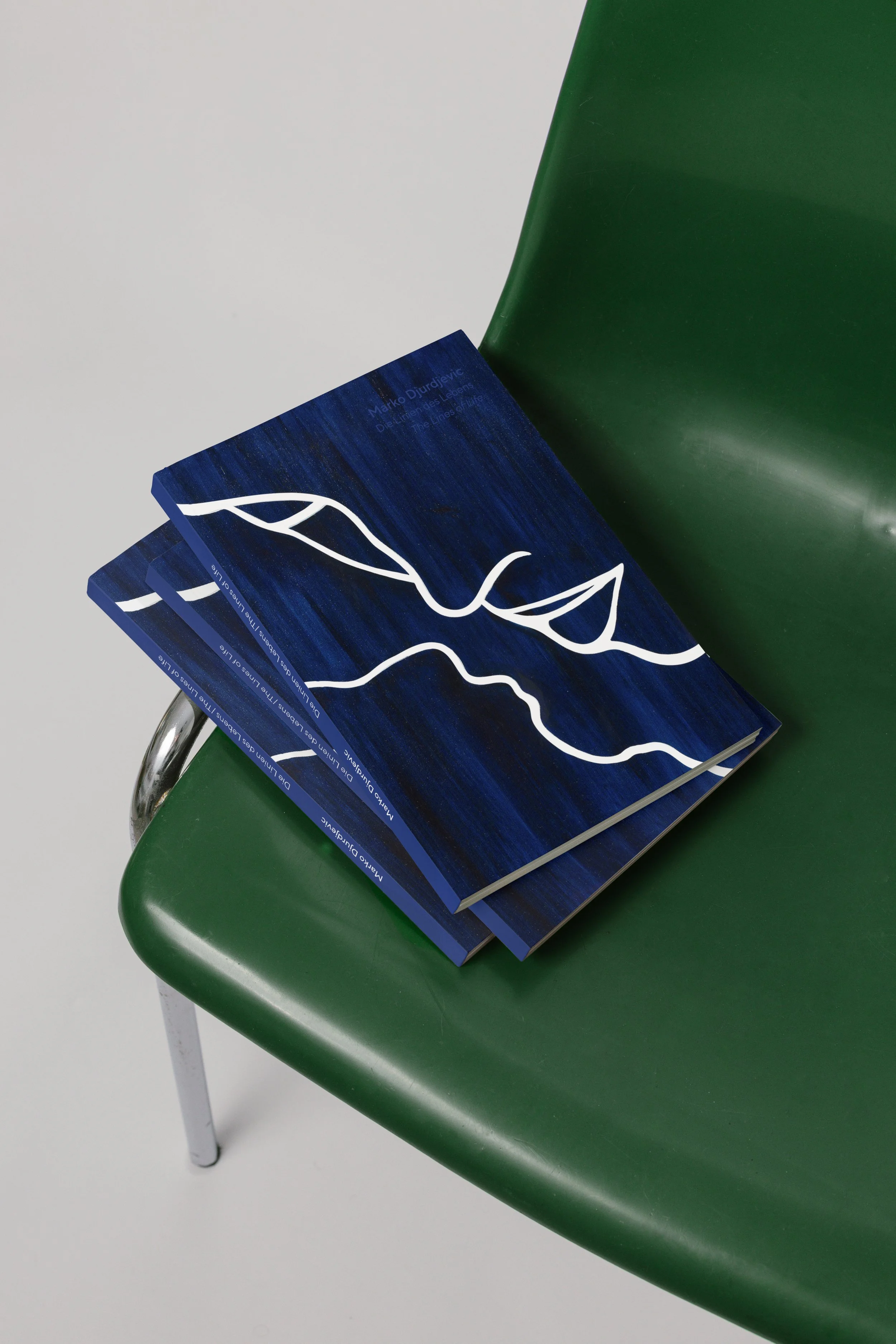 Drei blaue Bücher mit weißen Linien auf einem grünen Stuhl