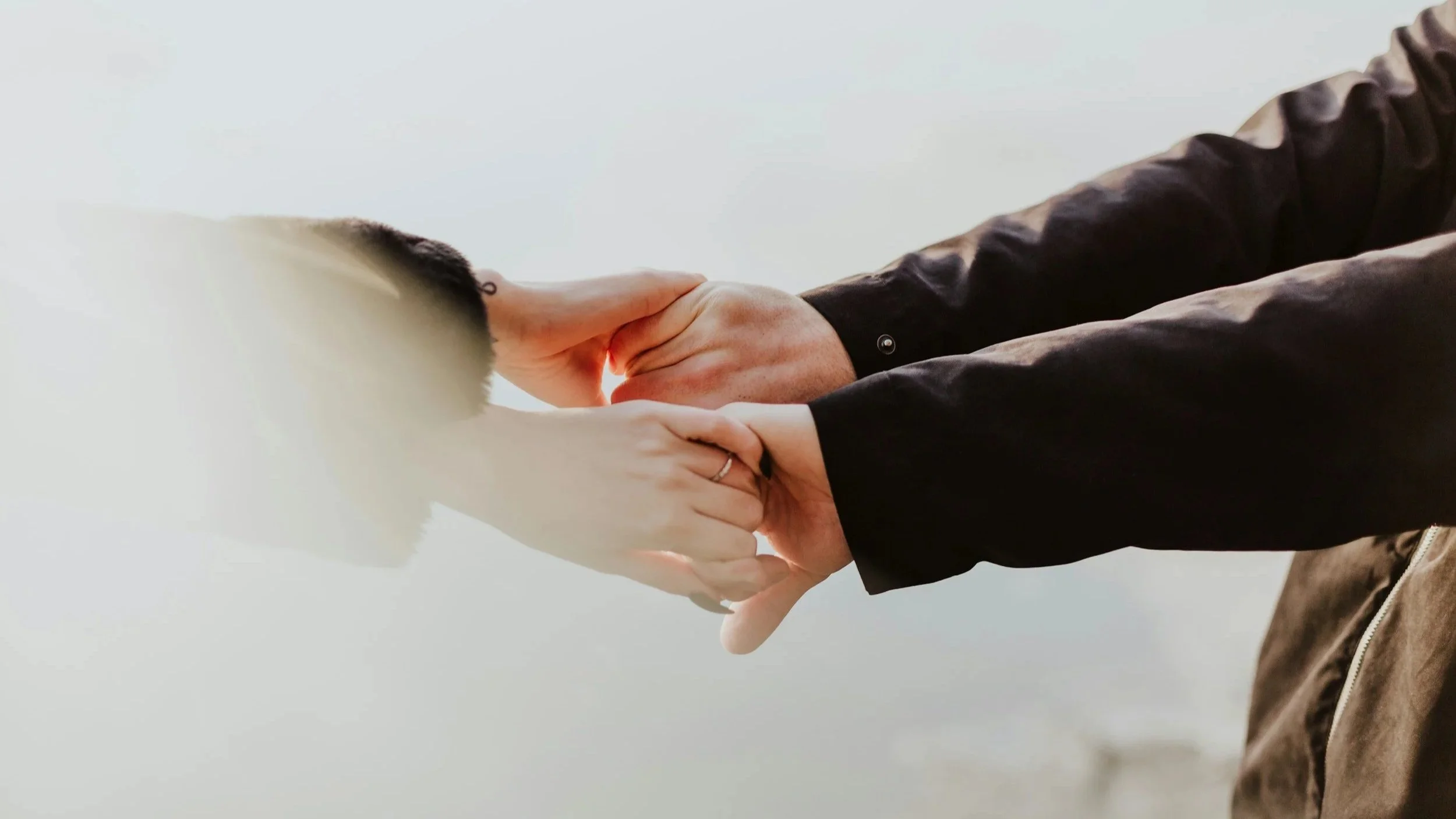 Two people holding hands, one person touching the other's face, with both wearing dark and light clothing respectively.